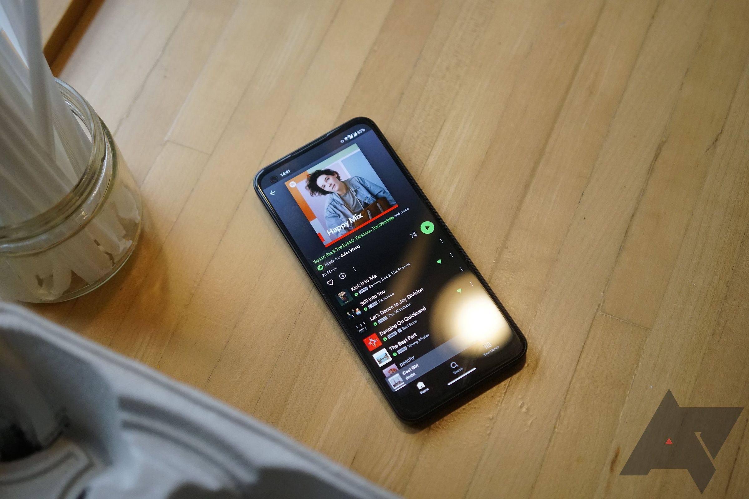A phone with the Spotify app open to a playlist sits on a wood table.