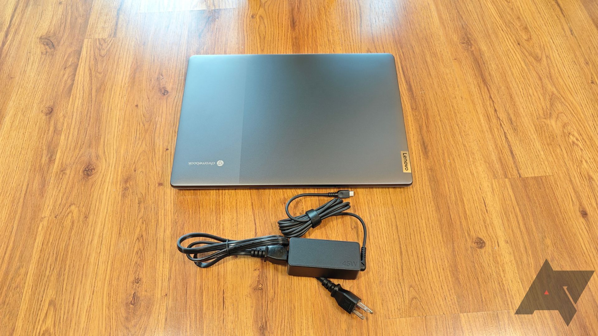 A Lenovo IdeaPad 5i Chromebook on a wooden floor with it's charger in front of it