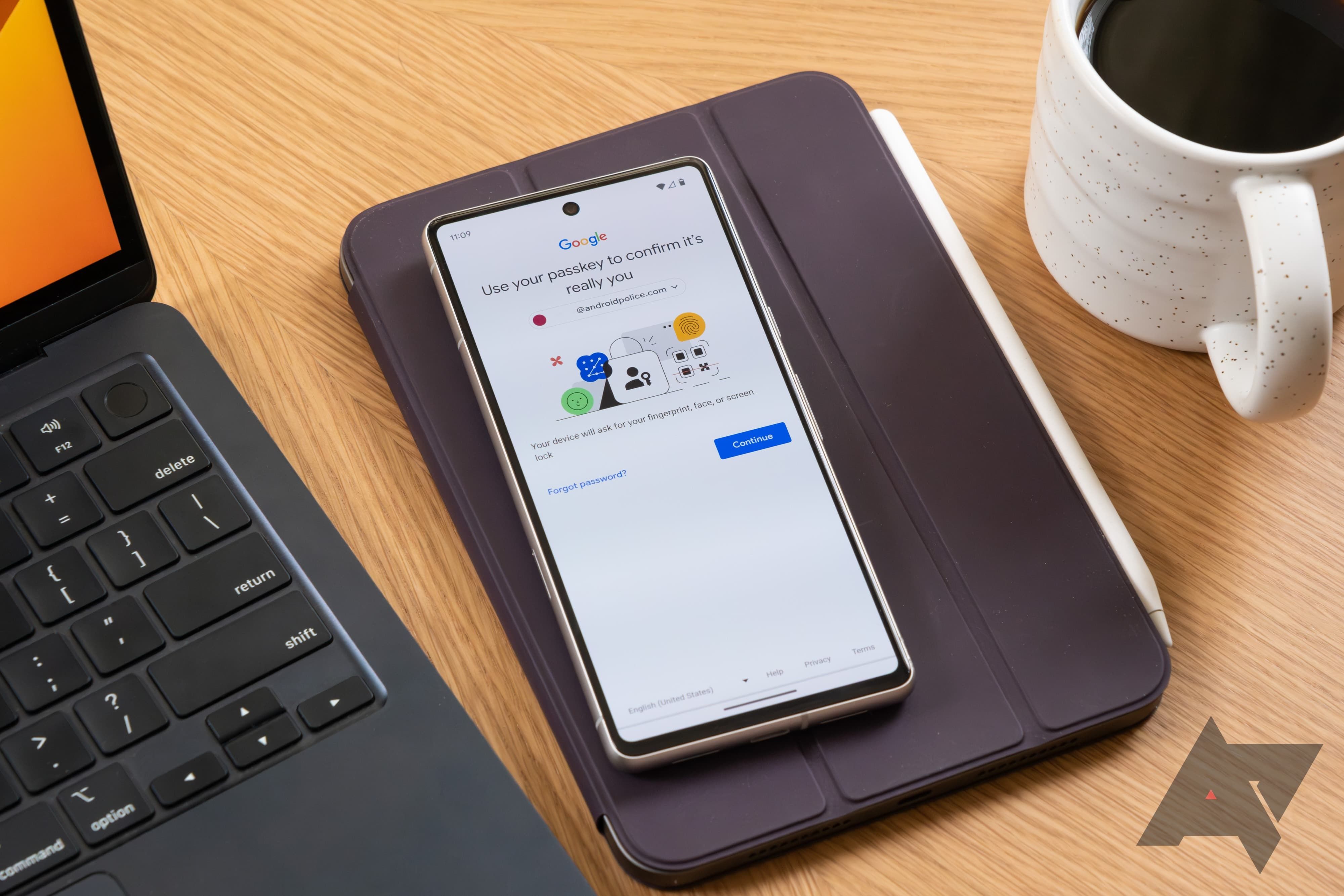 A phone with the Google Passkey setup screen sits on a leather tablet case. It is flanked by laptop and coffee mug.
