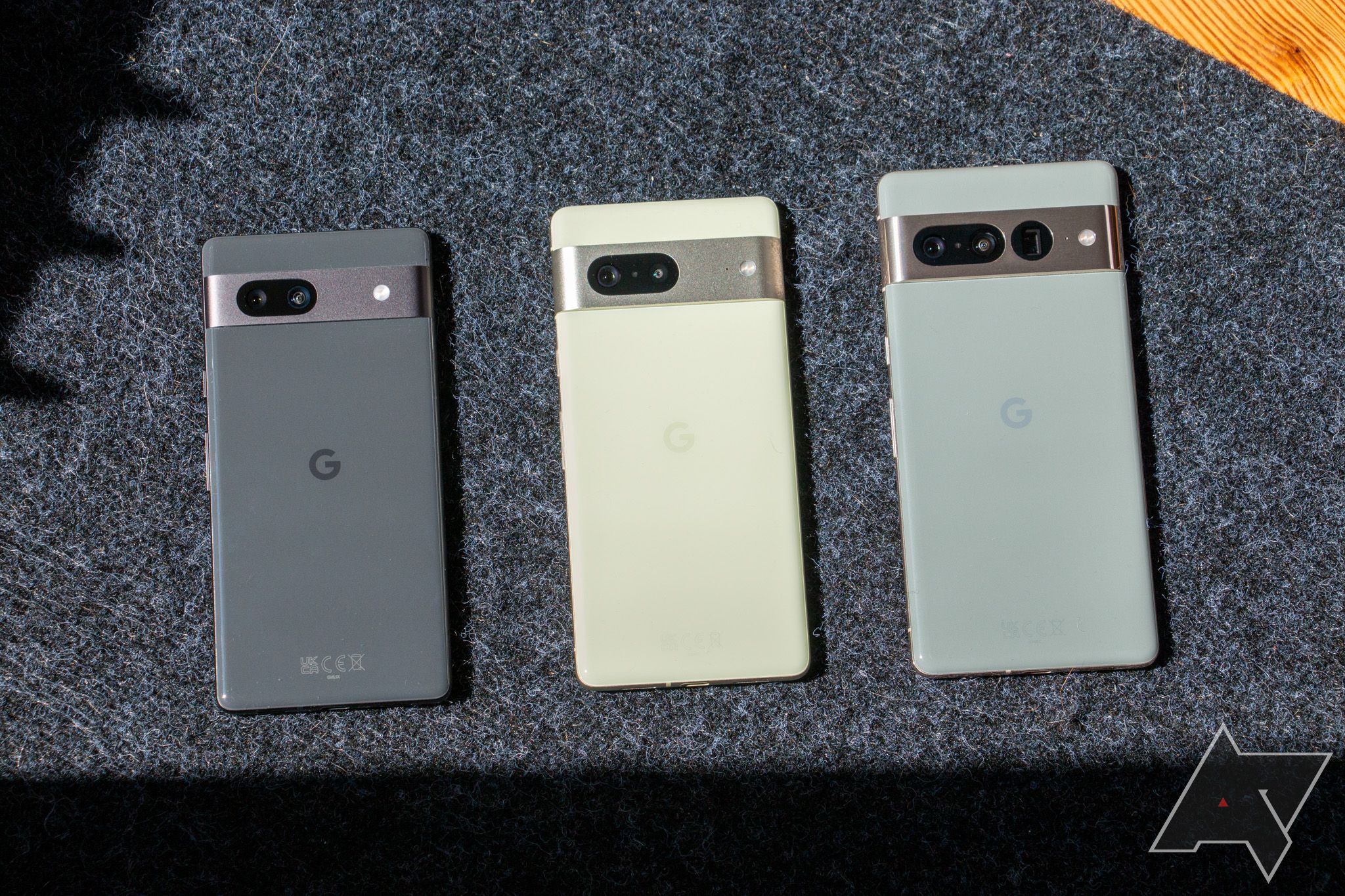 The Pixel 7a resting on gray fabric to the left of the Pixel 7 and Pixel 7 Pro.