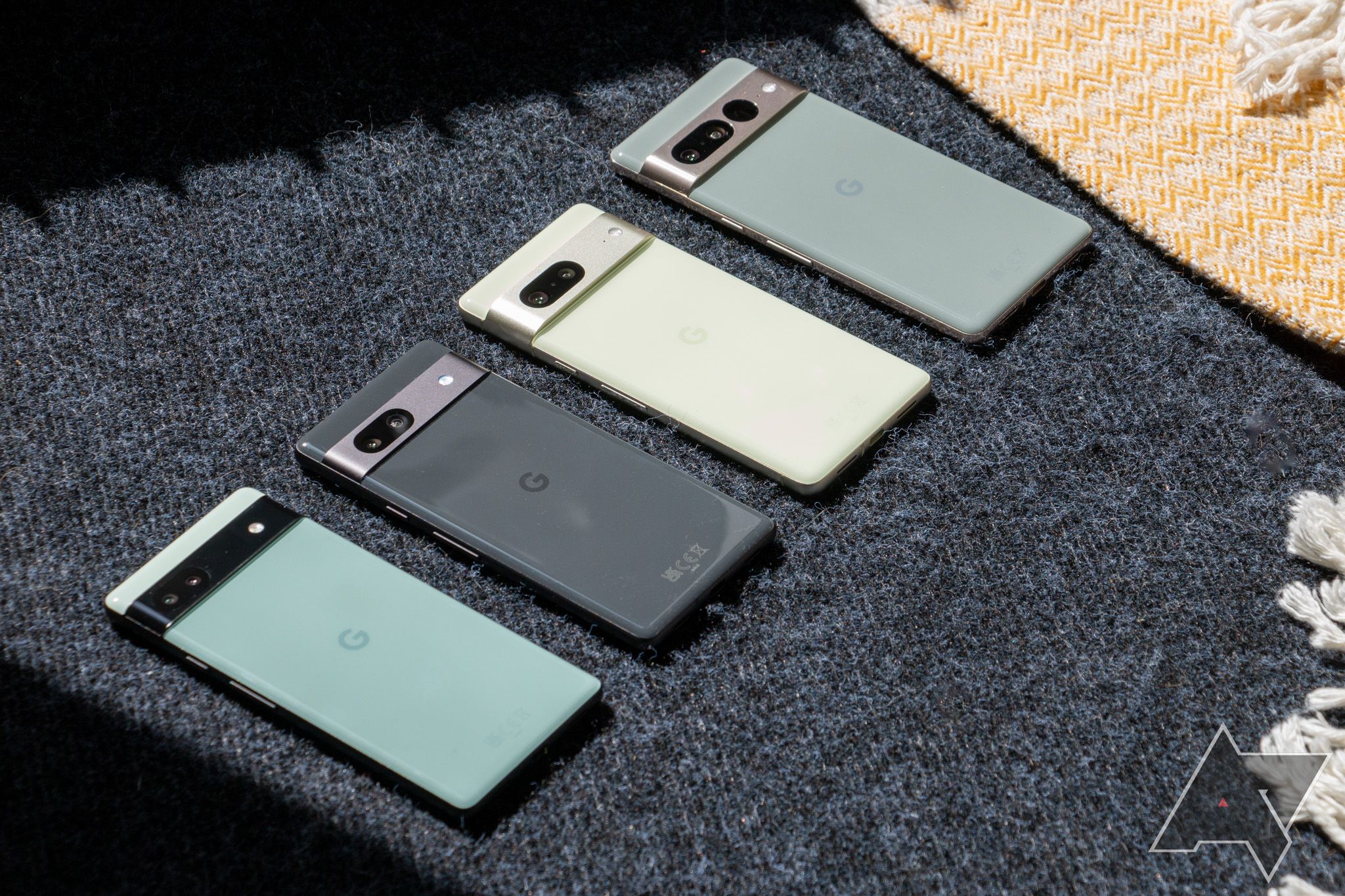 Several generations of Google Pixel smartphones lined up on a piece of fabric.