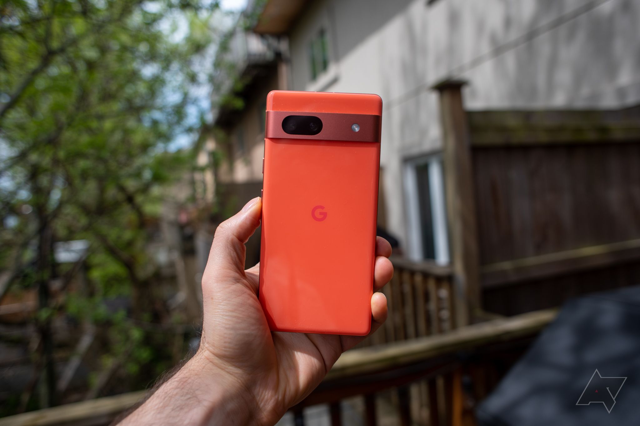 The Pixel 7a in coral outdoors with a fence behind it