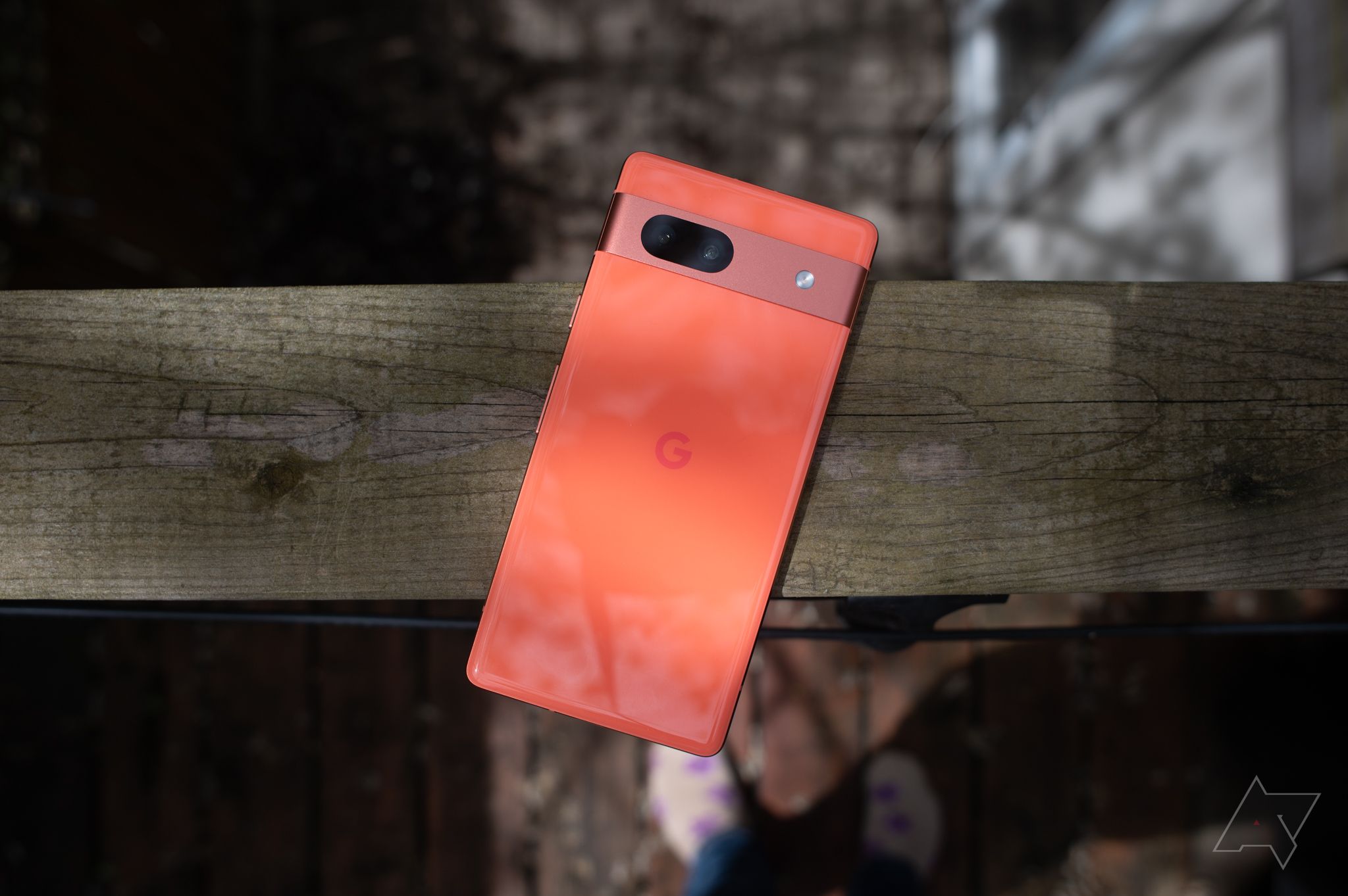 A coral Google Pixel 7a balanced on a wooden beam.