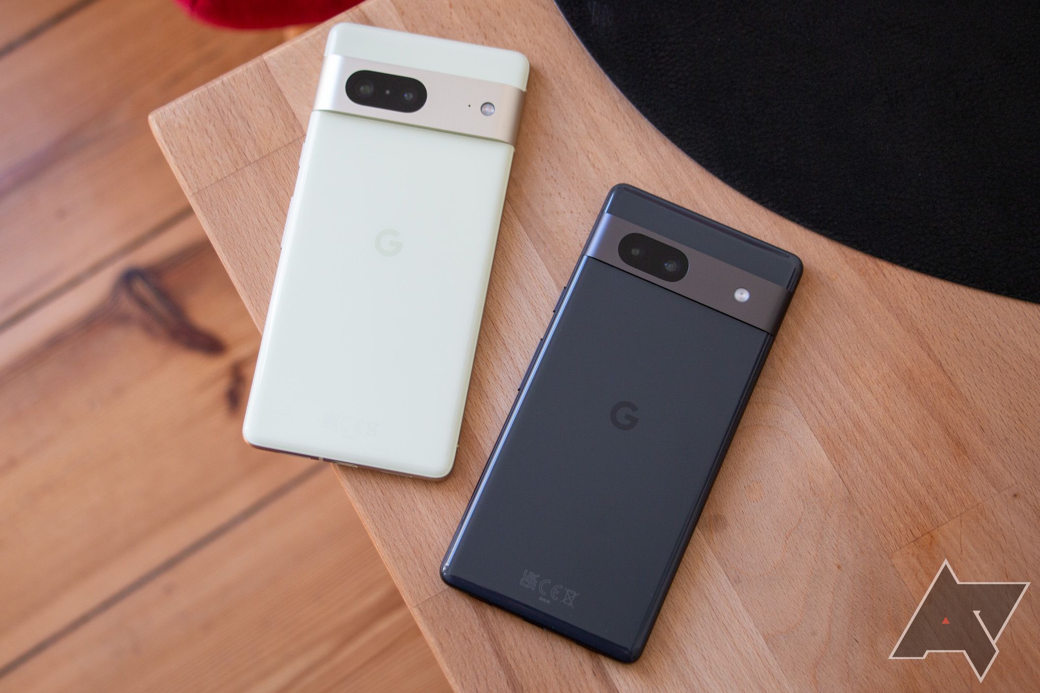 The Pixel 7a next to the Pixel 7 on a wooden table.
