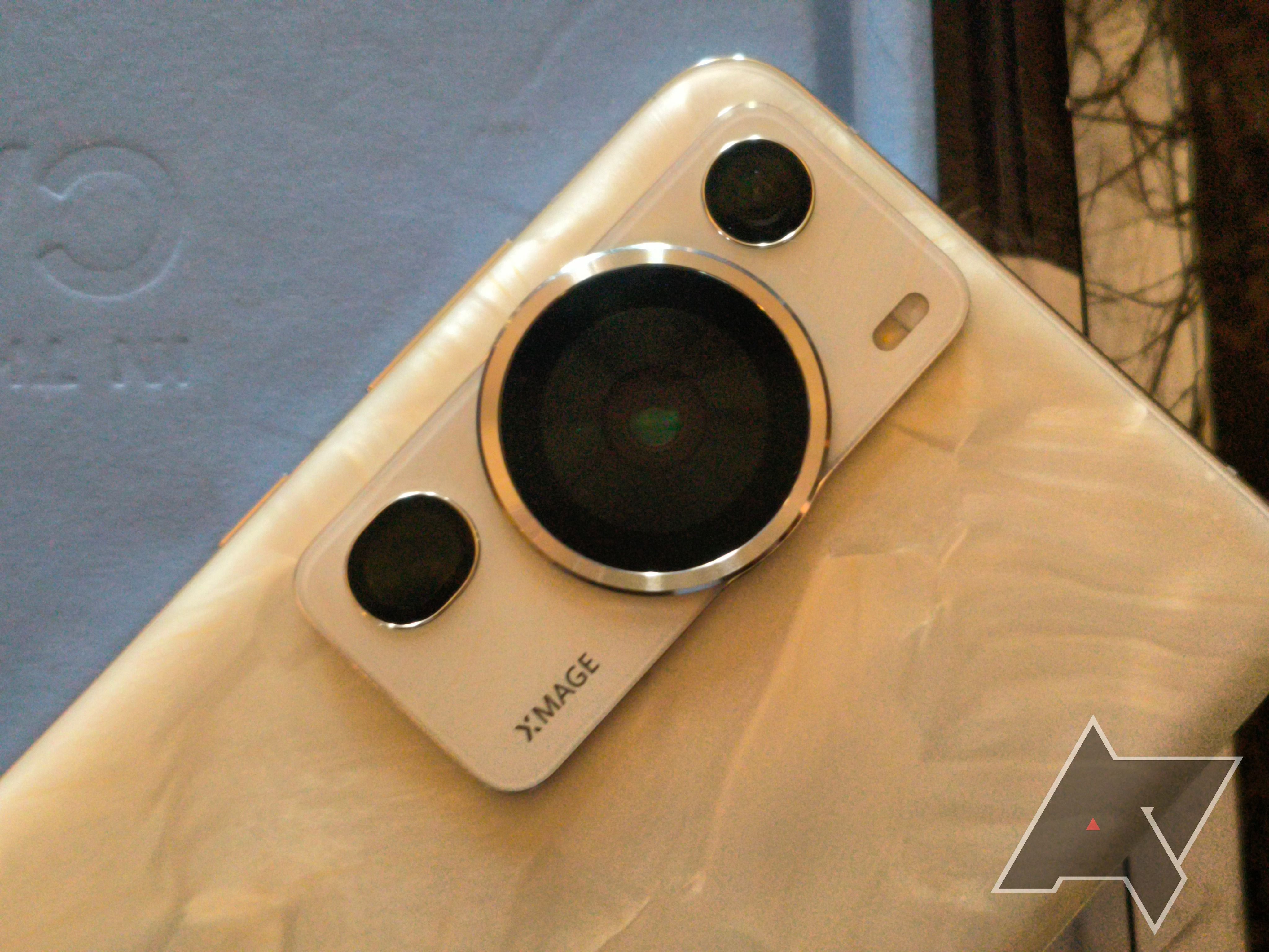 A gold Huawei phone's camera module on top of a grey notebook sitting on a marble table.