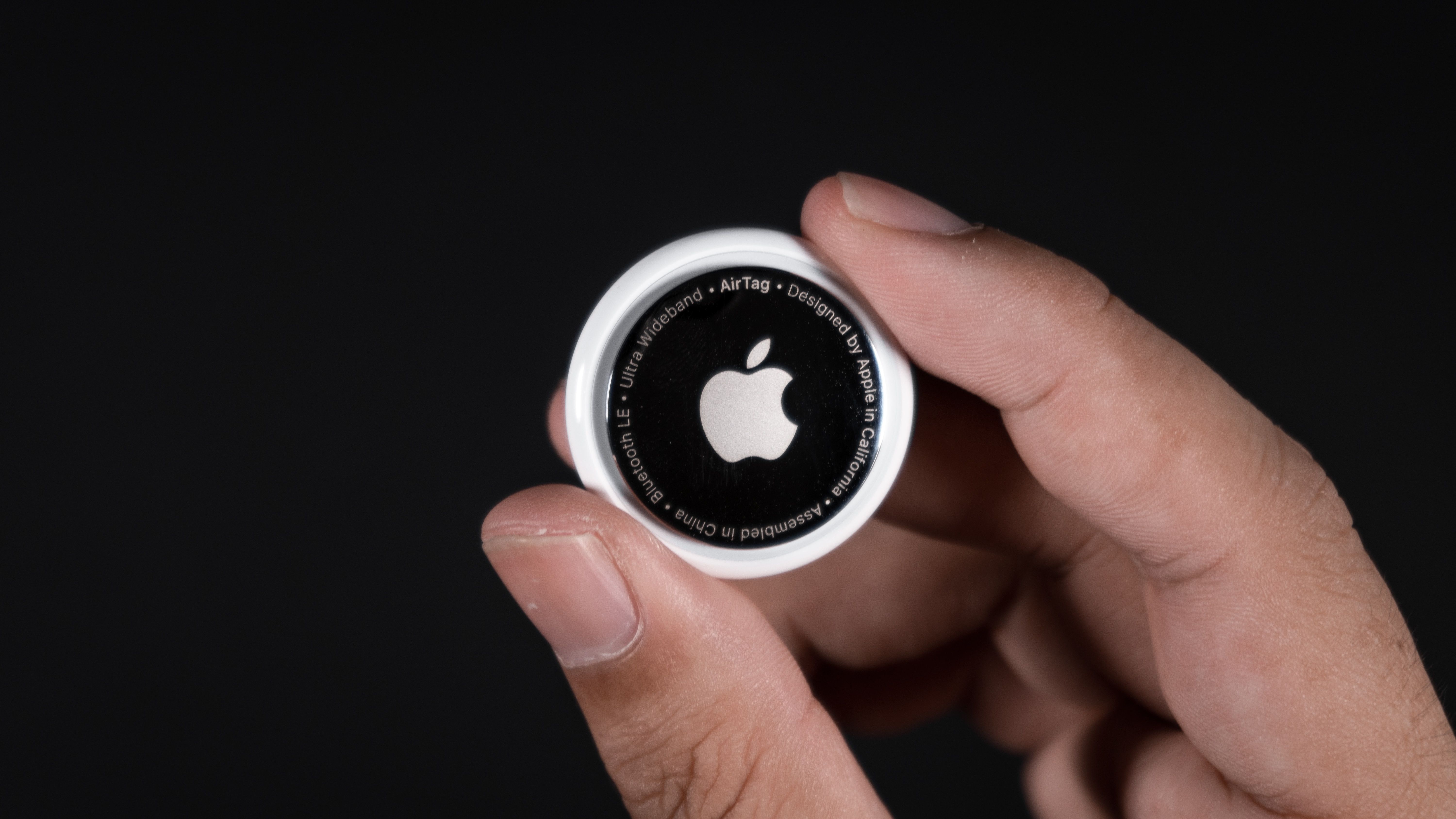 Close-up photo of an Apple AirTag held in hands against a black background