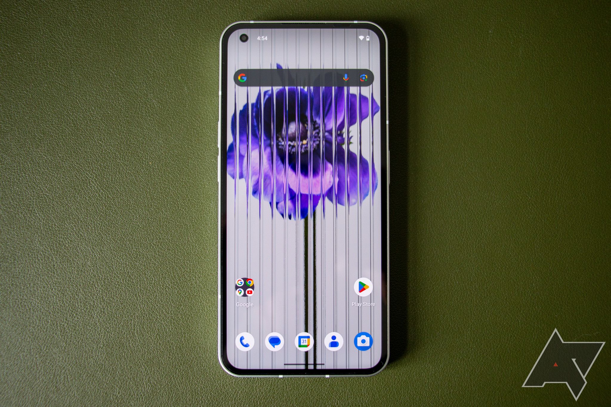 The Nothing Phone 1 lying on a green background with display turned on, showing the Android 14 beta launcher