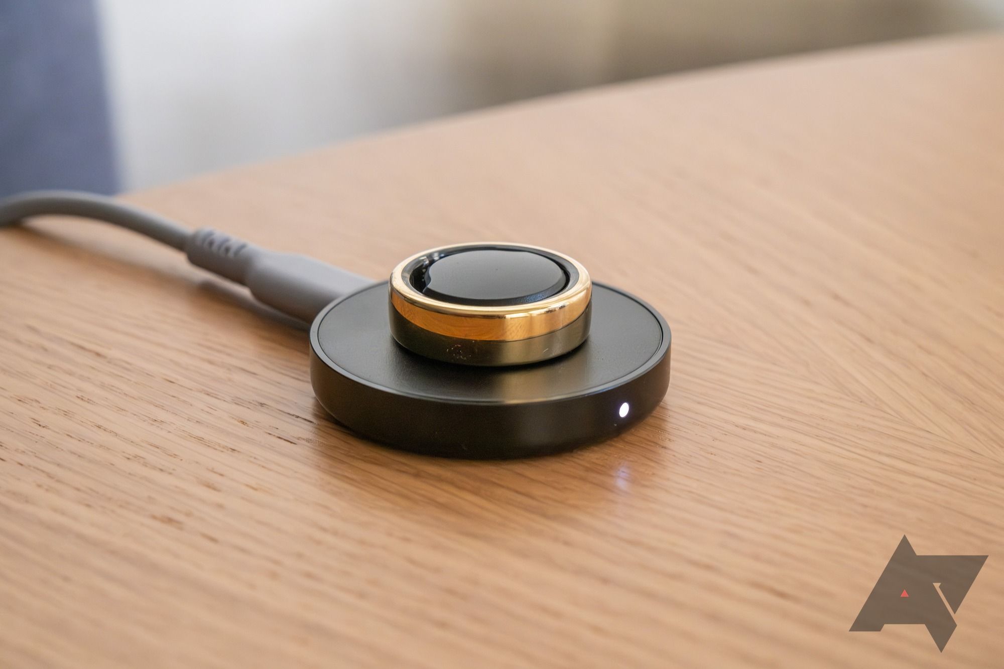 A gold smart ring sitting on a charger.