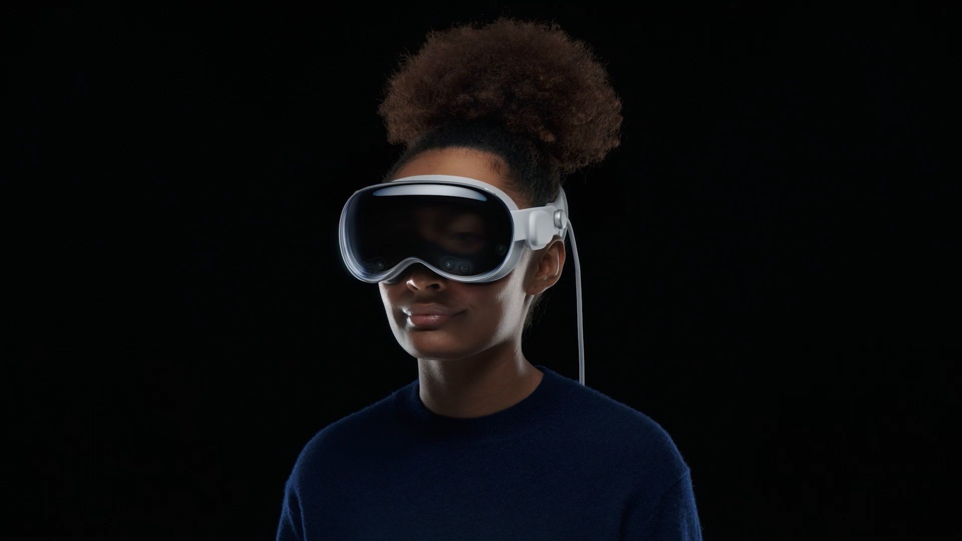 A woman wearing the Apple Vision Pro headset in front of a black background