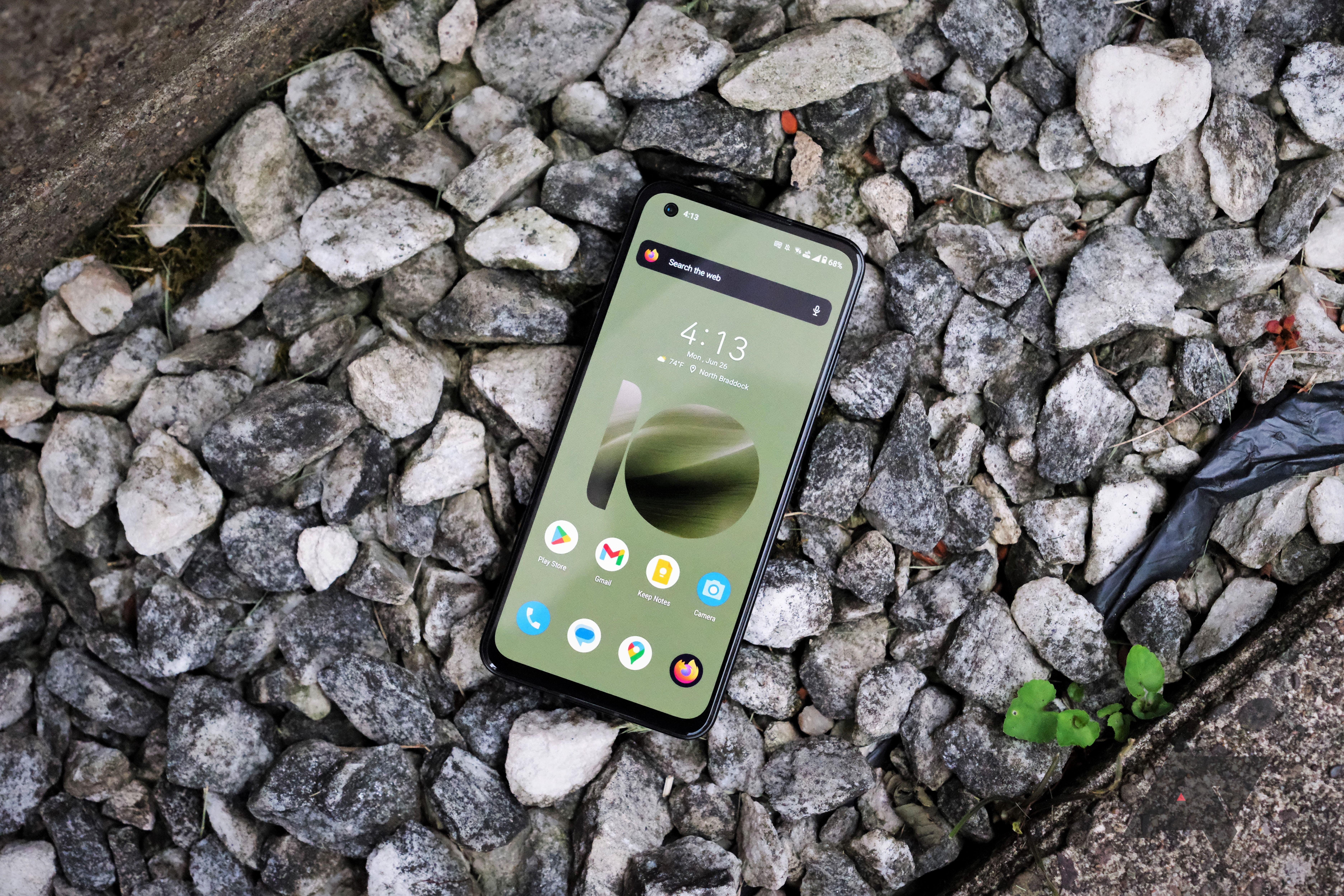 A smartphone with a green display rests on rocks.