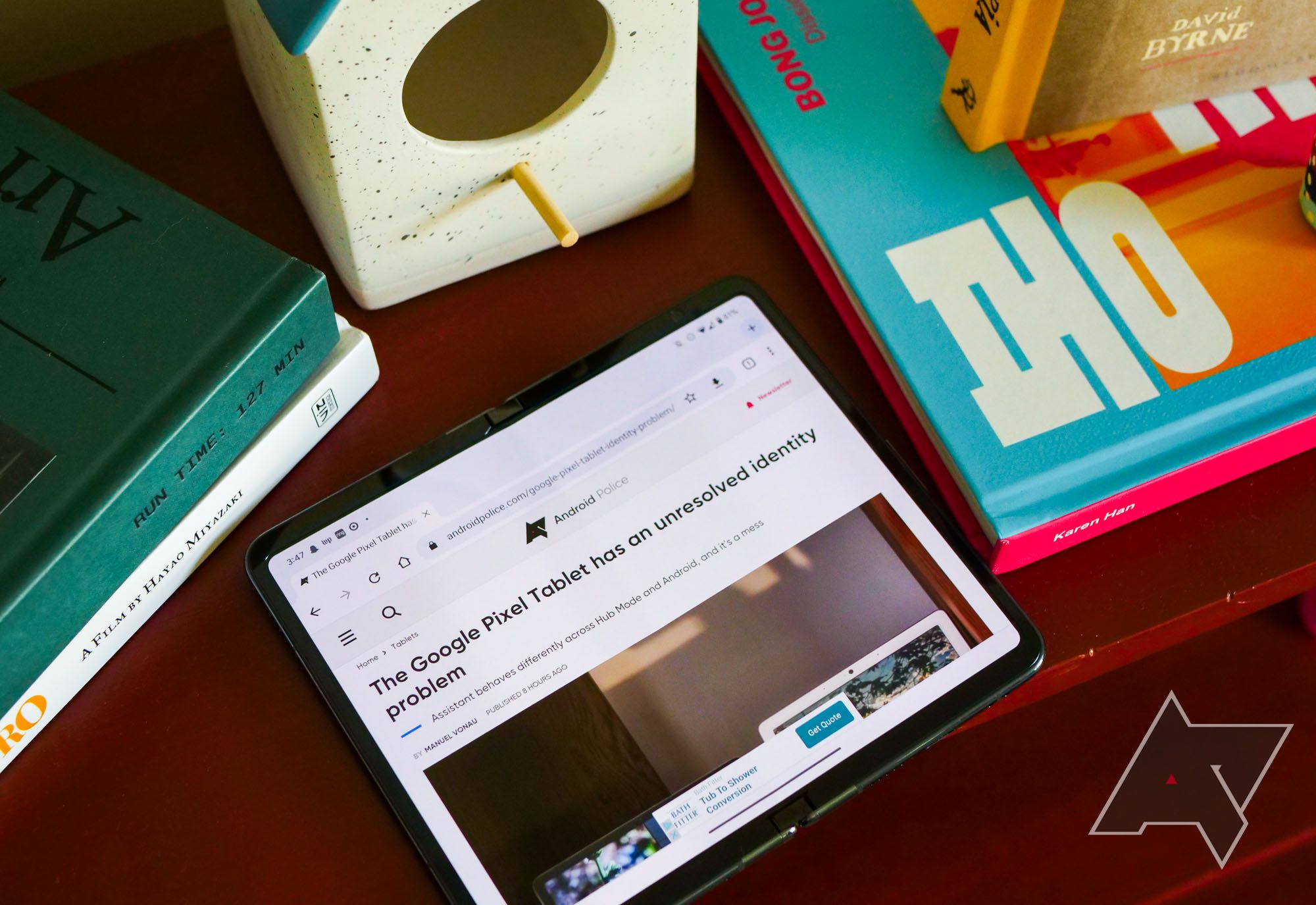 A foldable phone sits on a wooden desk, surrounded by various books.
