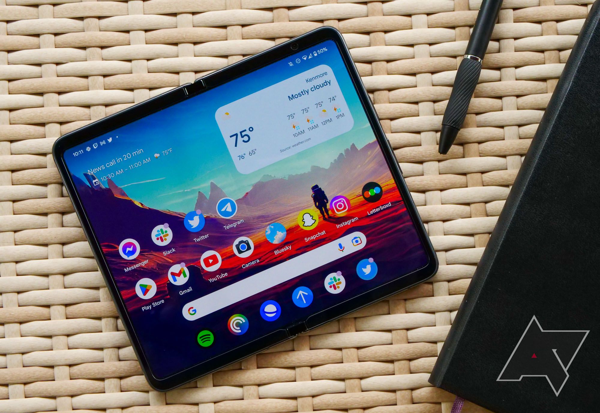 Google Pixel Fold on a wicker table with a notebook and pen next to it.