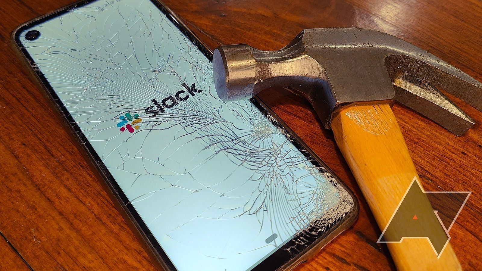 A smartphone displays the Slack logo through a cracked display while a hammer rests on the screen