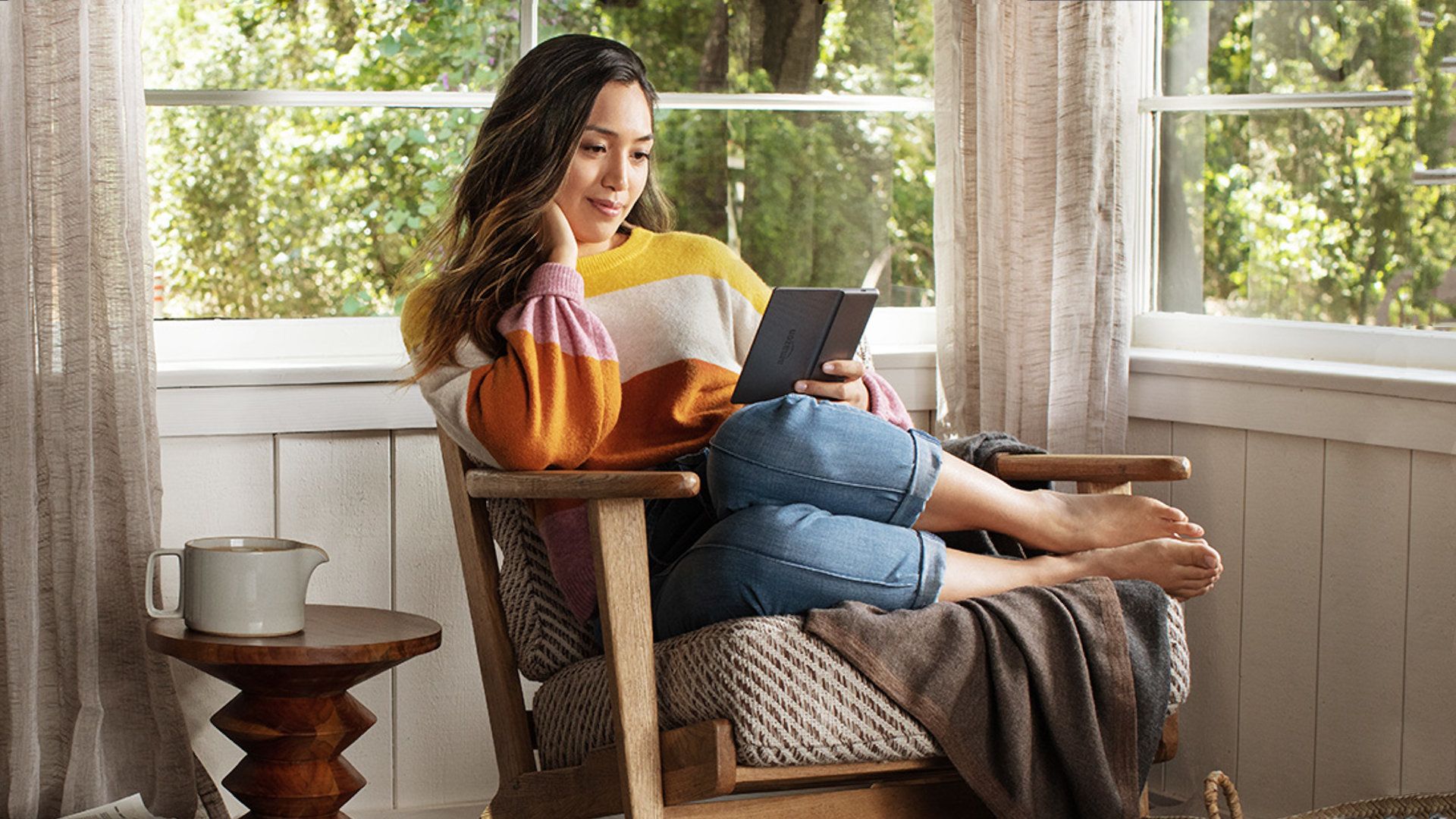 A model sits sideways in a chair reading with a Kindle Oasis.