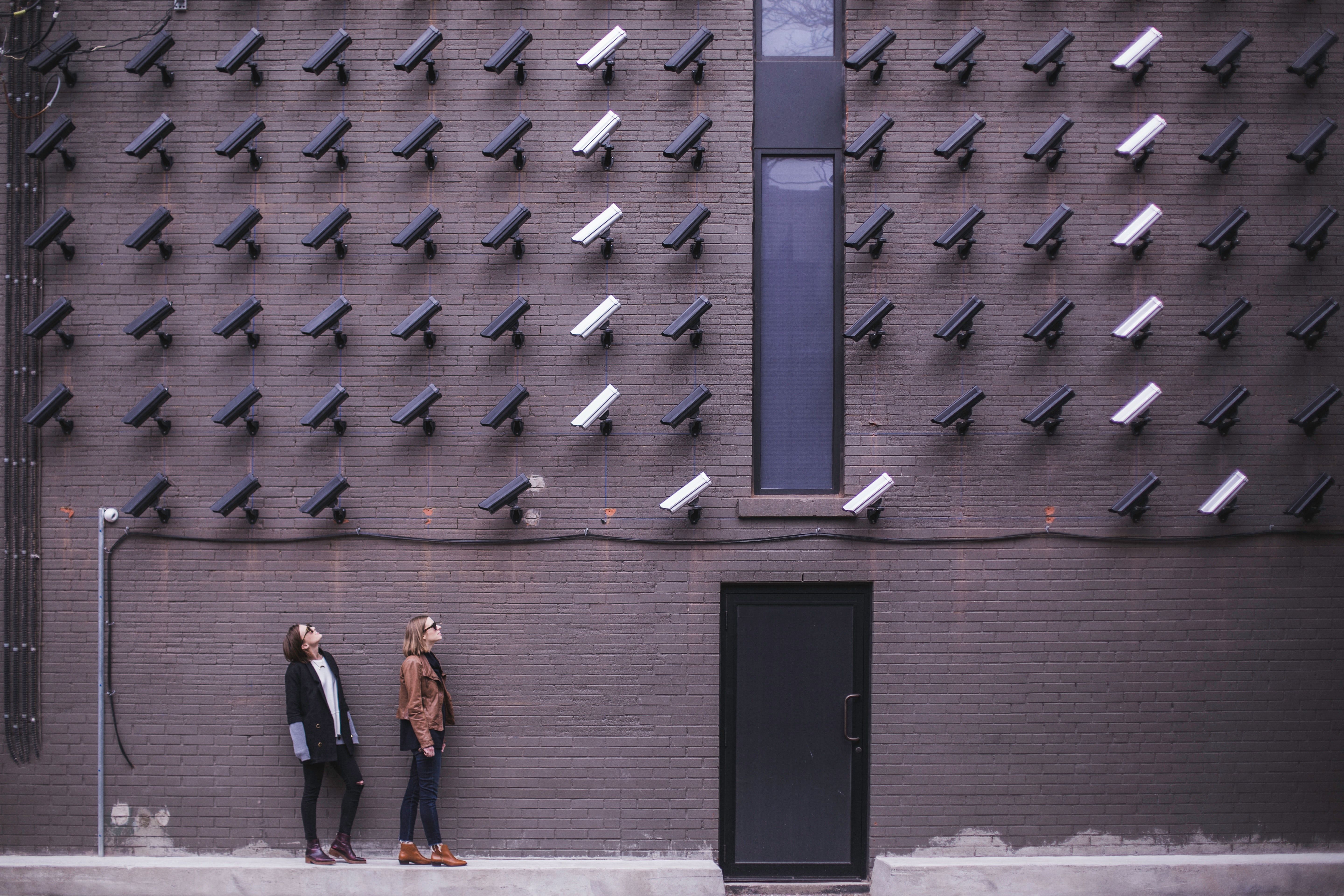 Two people standing below dozens of closed-circuit cameras