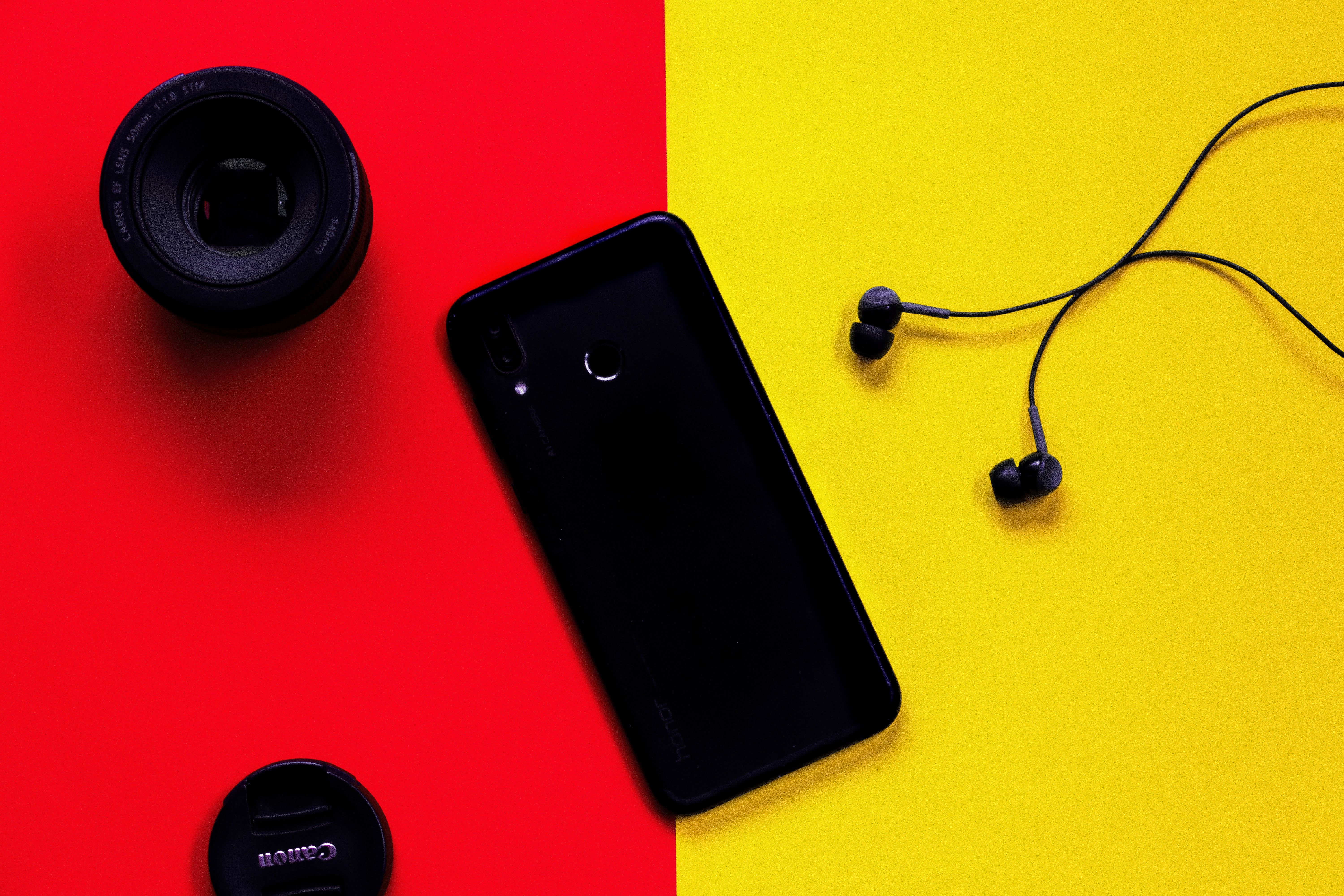 Black Smartphone Besides Earphones and Camera Lens