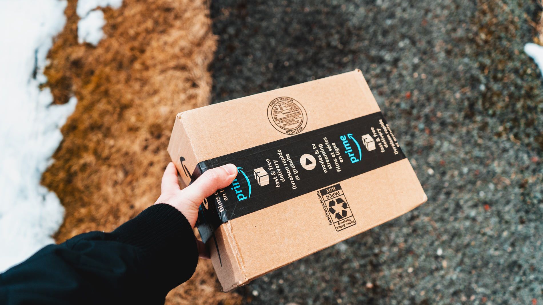 A person holds a small box sealed with Amazon Prime packing tape.