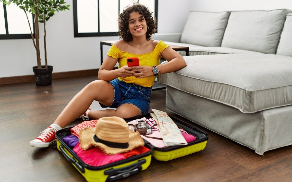 A female traveler using her phone while unpacking at a hotel