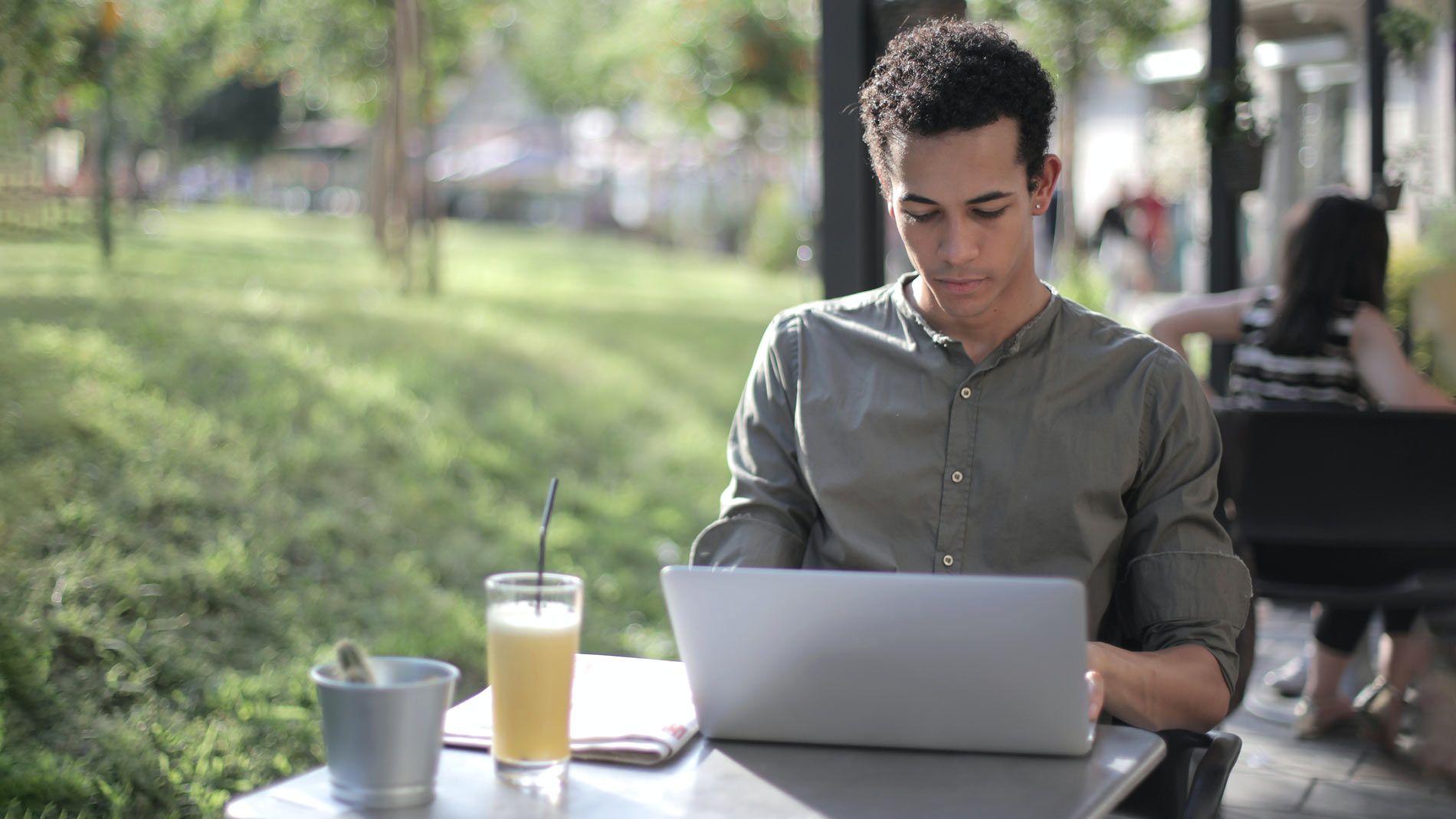 A person sits outside with a drink looking at a silver laptop.