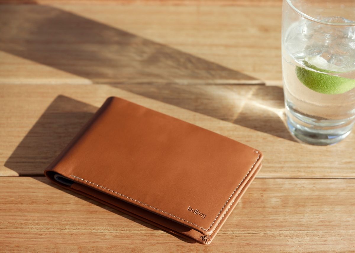 The bellroy leather wallet on a desk next to a cup of water