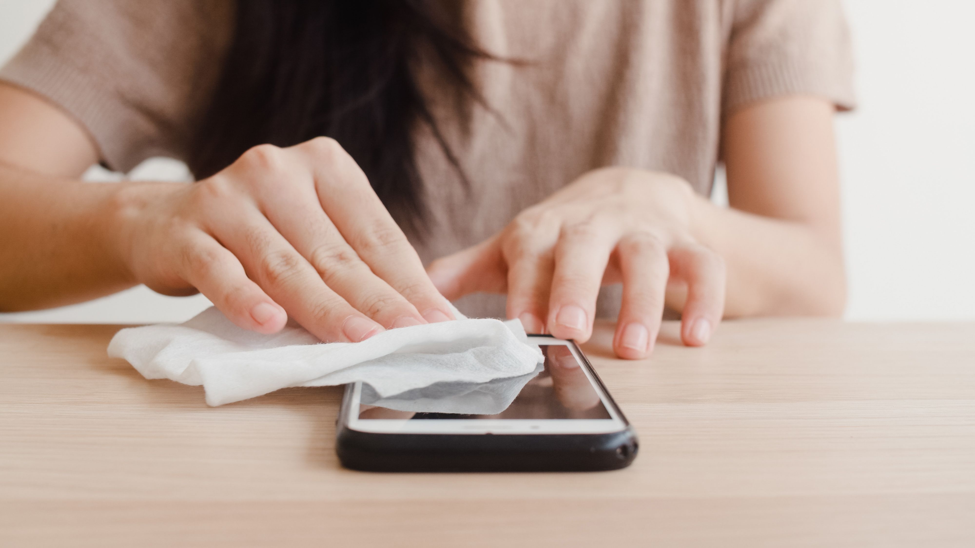 a woman gently wiping the entire screen of her phone using a microfiber cloth