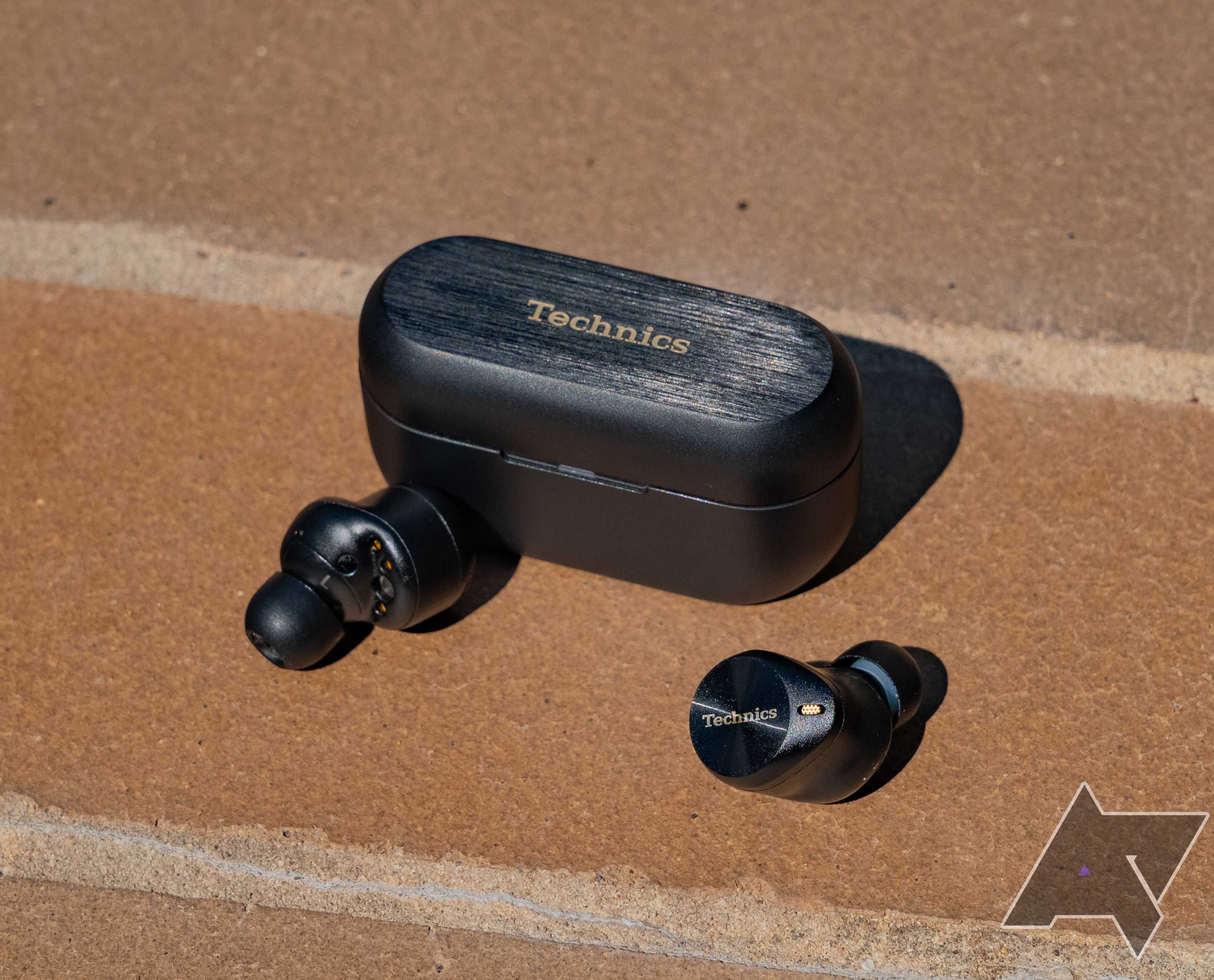 The Technics AZ80 earbuds sitting on a brick surface in front of the closed charging case