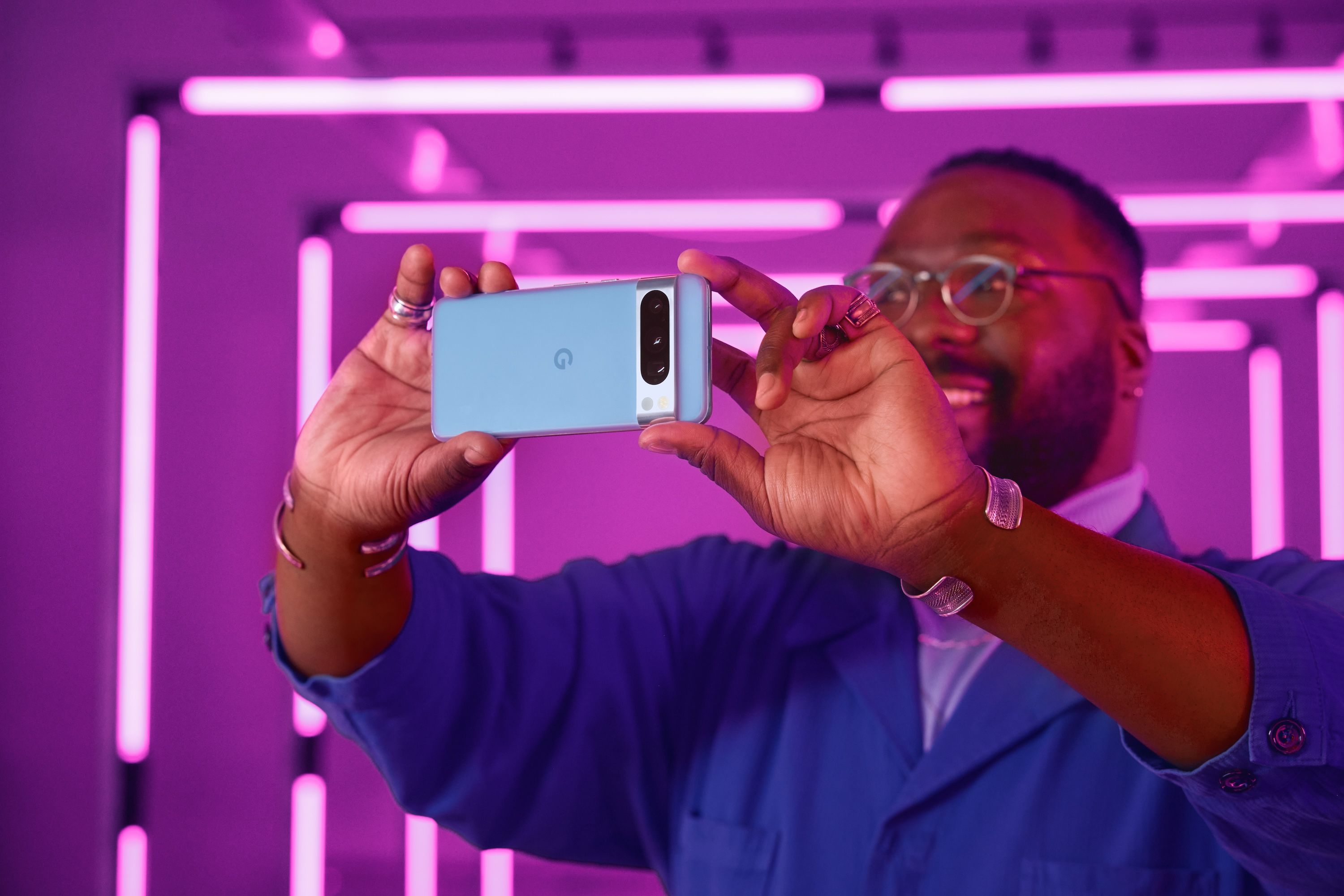 A man holds a blue Google Pixel 8 Pro in front of a purple background.