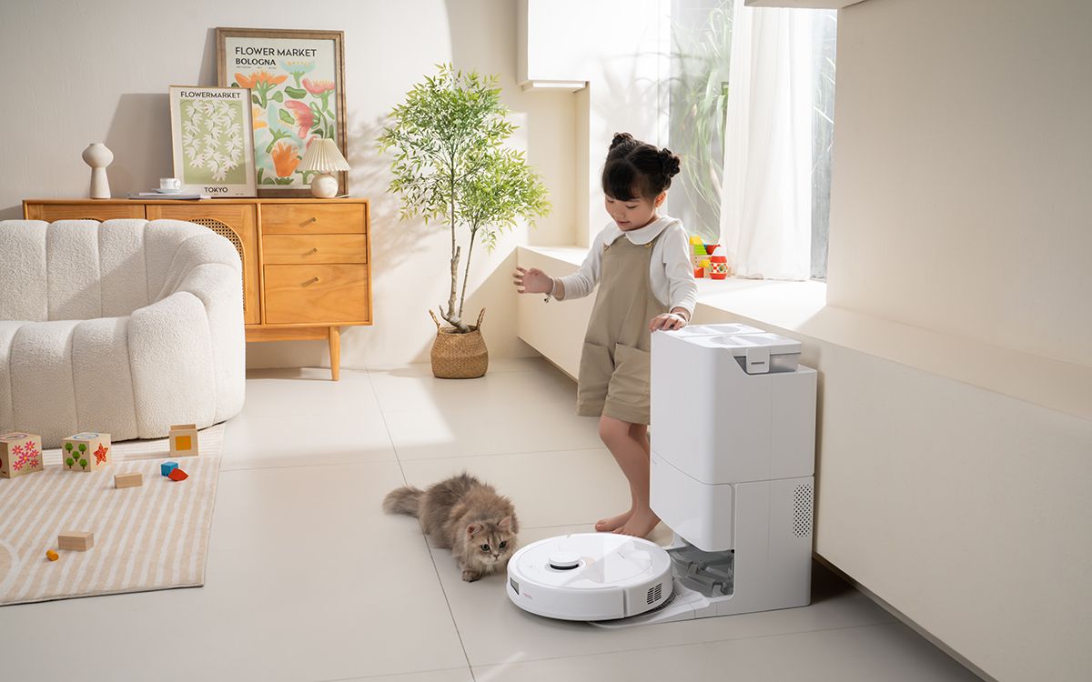 A little girl and a cat watch a white robot vacuum