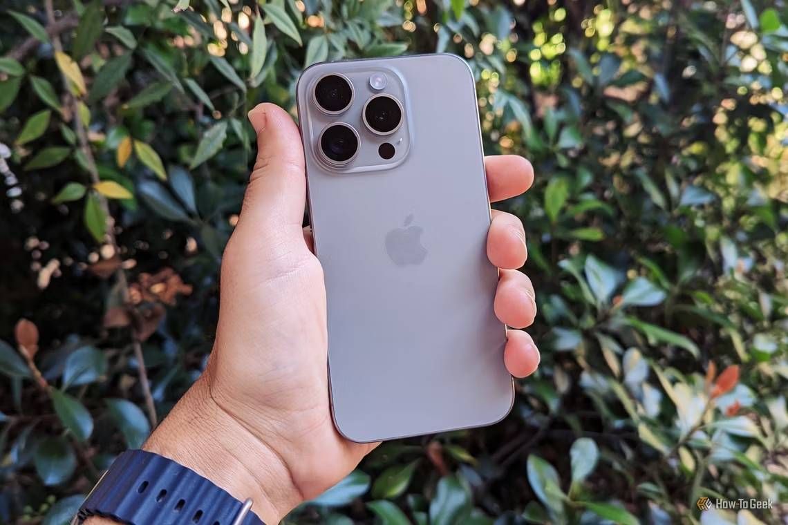 An iPhone 15 Pro held up in front of a hedge