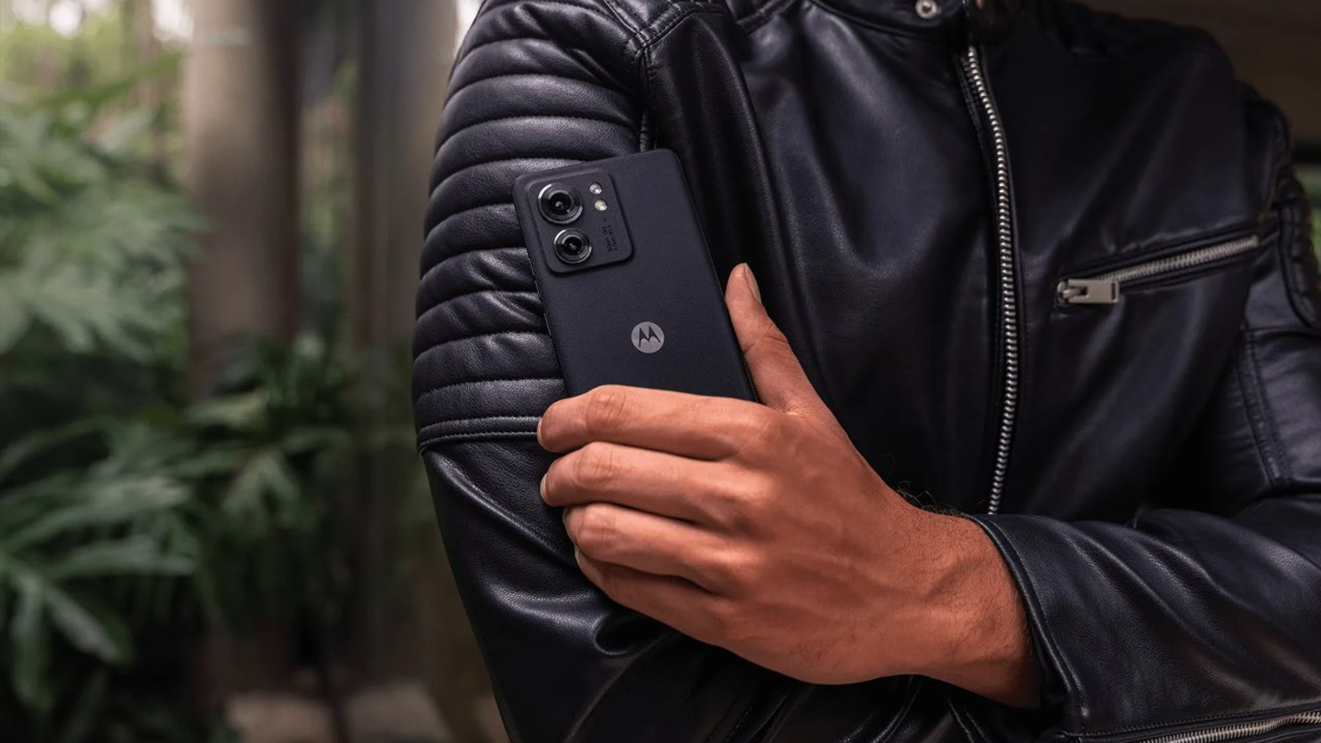 Motorola edge (2023) held by a person in a leather jacket against a forested background
