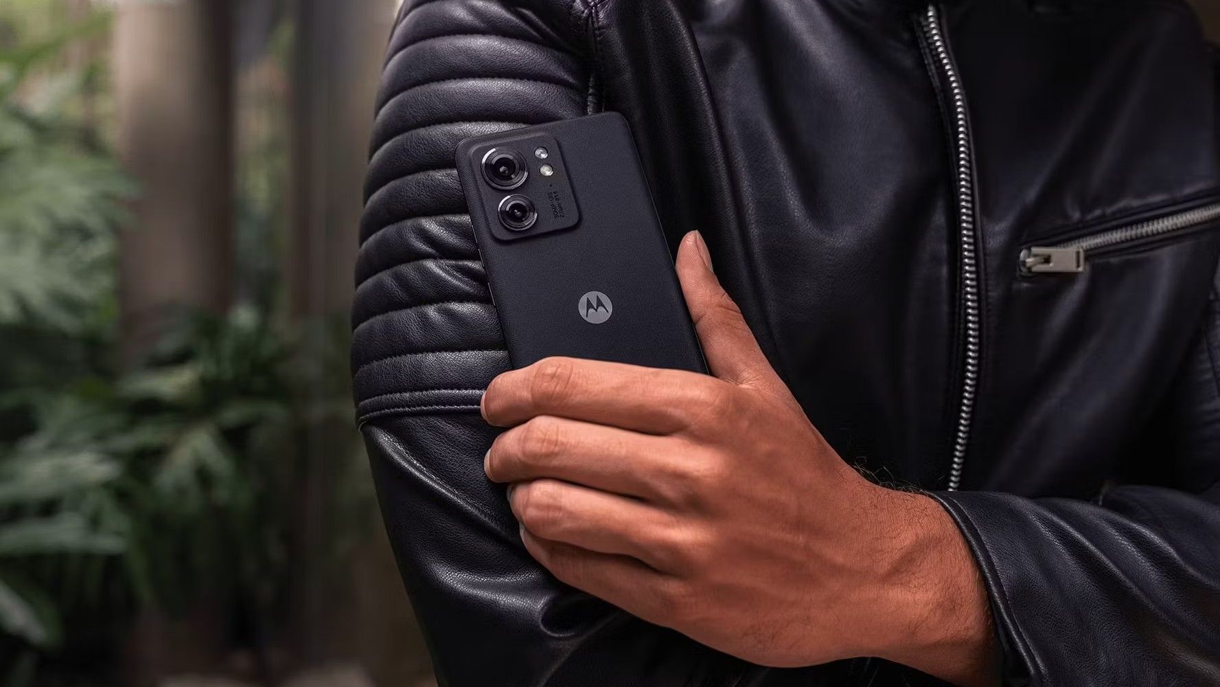 A man wearing a black leather jacket and holding a Motorola Edge (2023) phone
