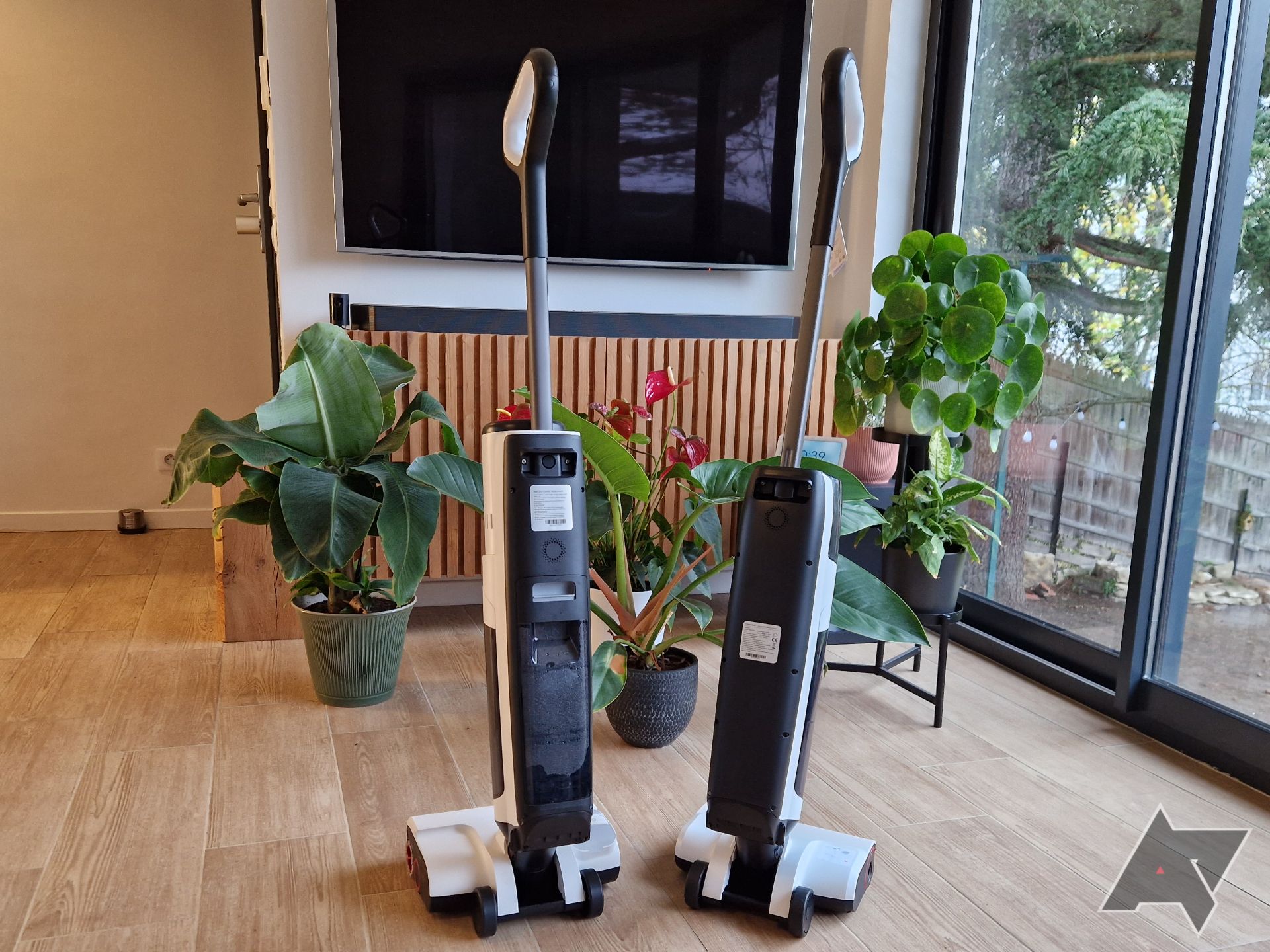 Picture of the Roborock Dyad Pro Combo and Dyad Air (right) next to each other, with plants and a TV in the background