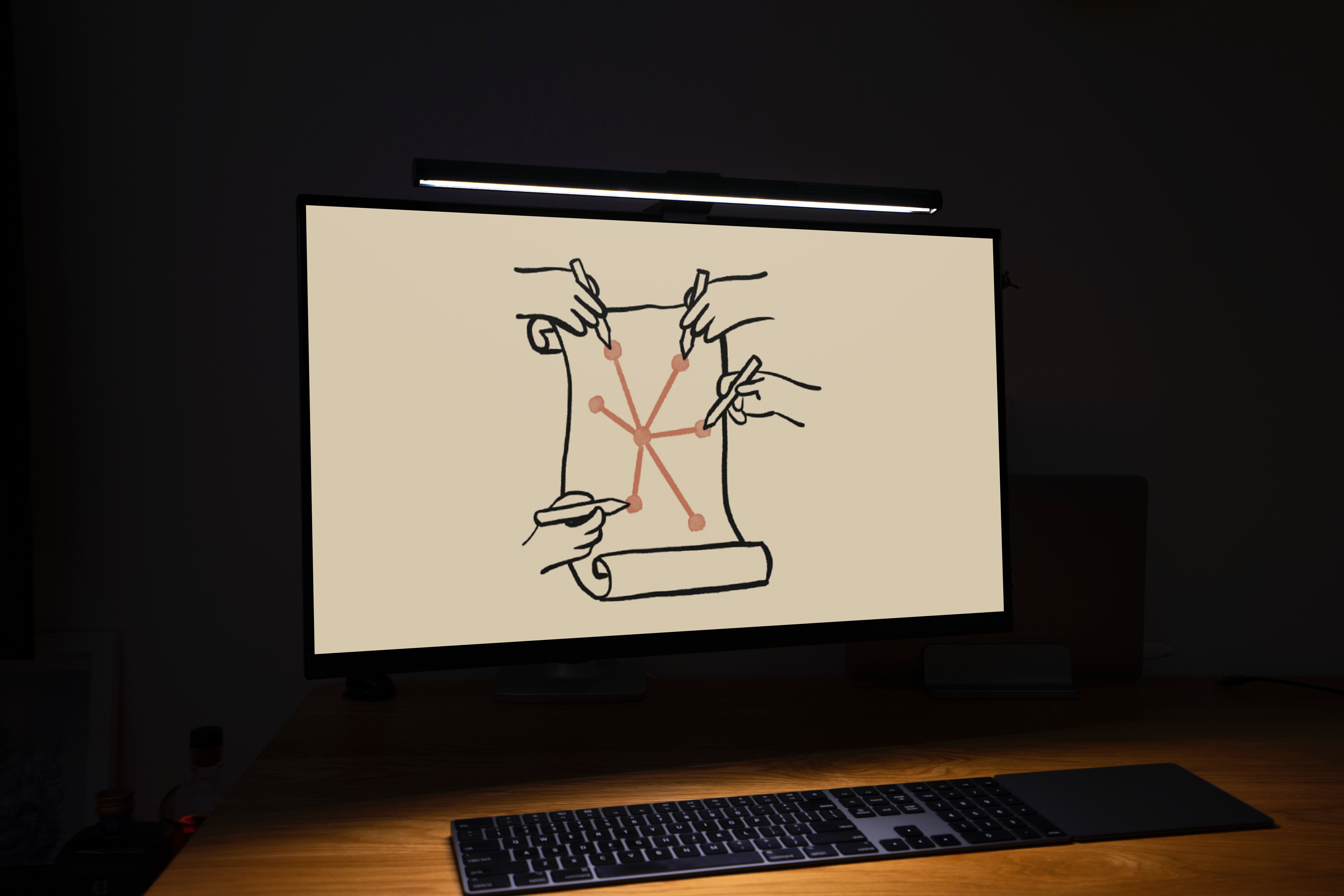 A monitor in a dark room displaying a hand-drawn image of four hands drawing on a scroll