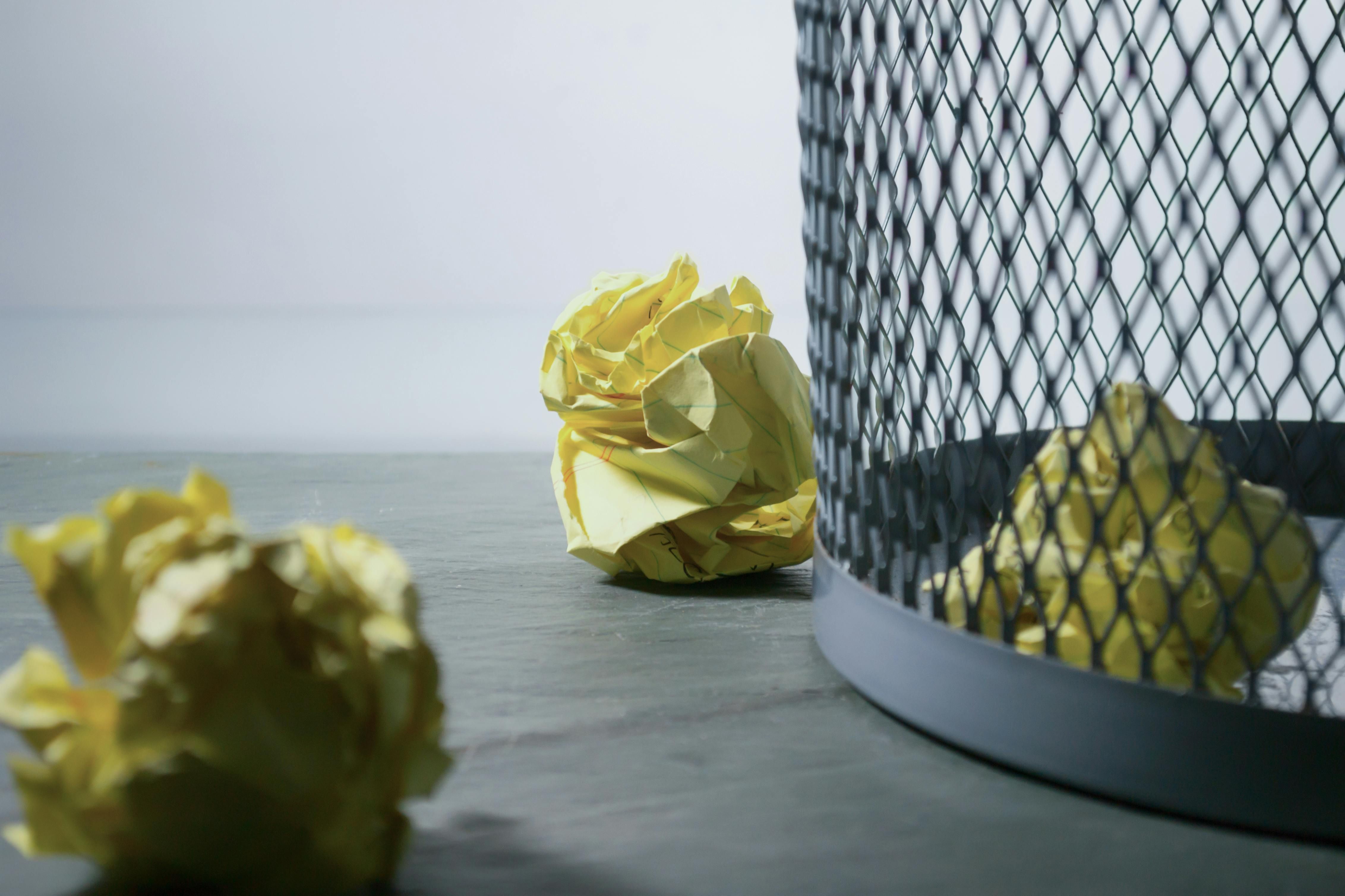 a wire trash can with yellow papers in and next to it