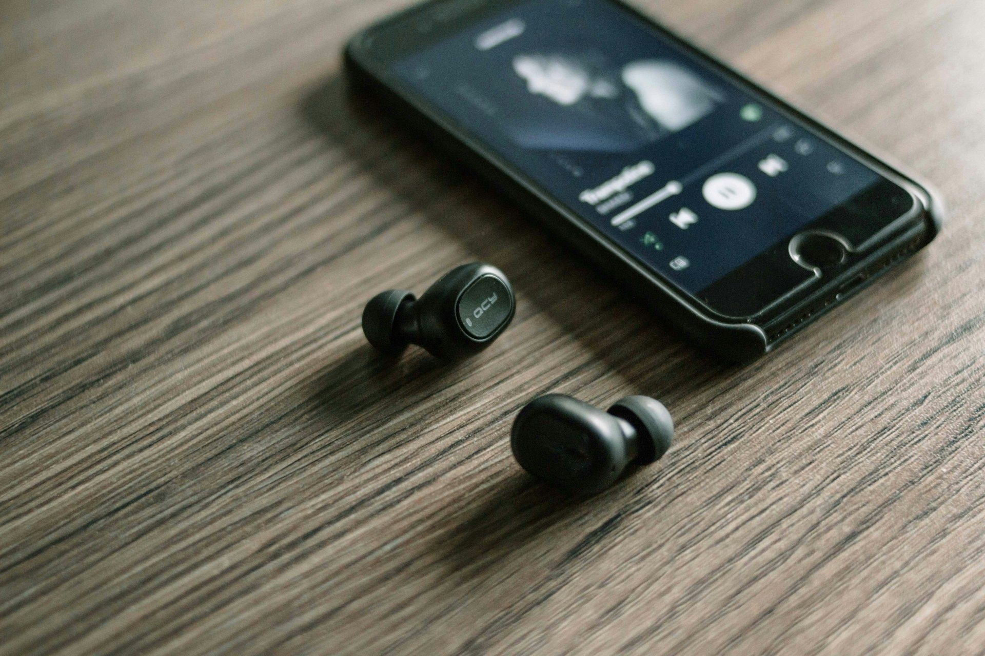 QCY earbuds on table next to a smartphone streaming music