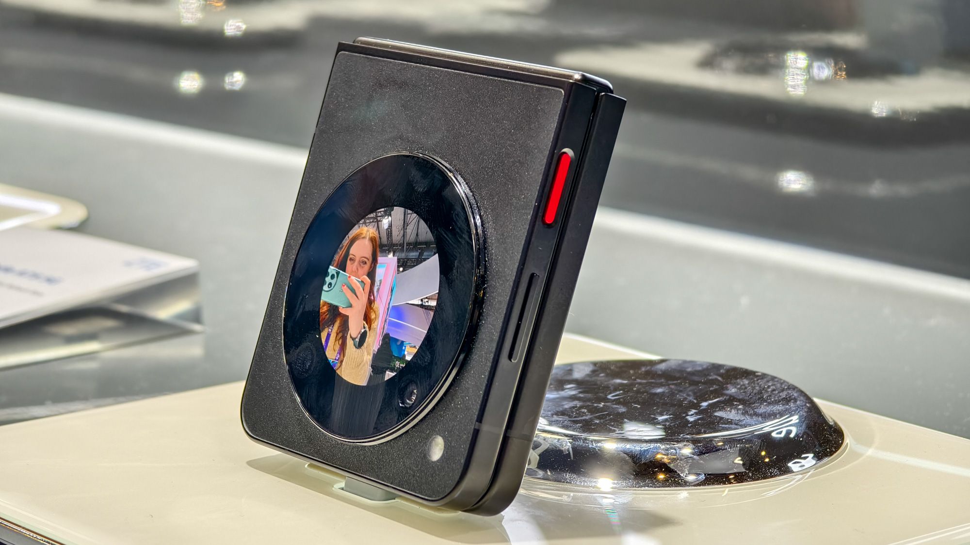Nubia Flip 5G in black at MWC 2024, with the camera viewfinder shown on the external display, showing a redheaded woman taking a photo with her phone