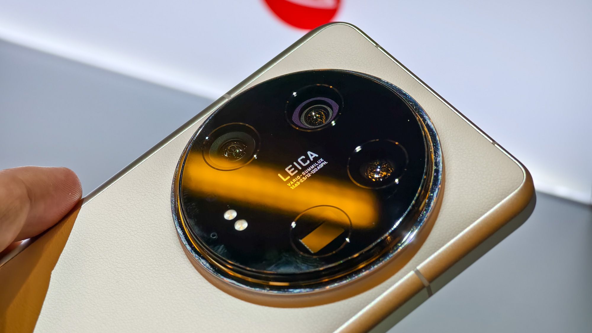 White Xiaomi 14 Ultra at MWC 2024, with a close-up on the Leica logo and cameras with orange light reflecting off