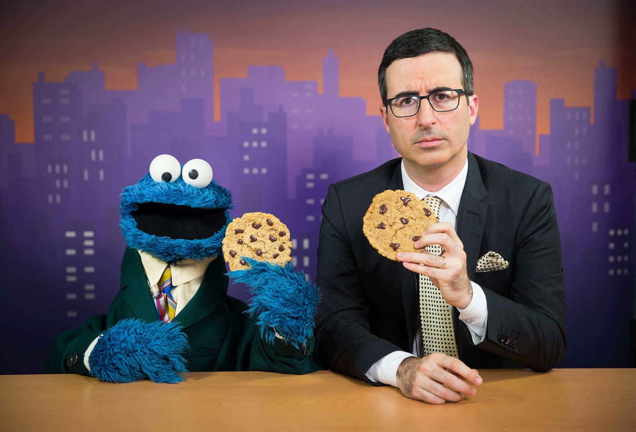 The Cookie Monster and John Oliver sitting at a desk holding cookies