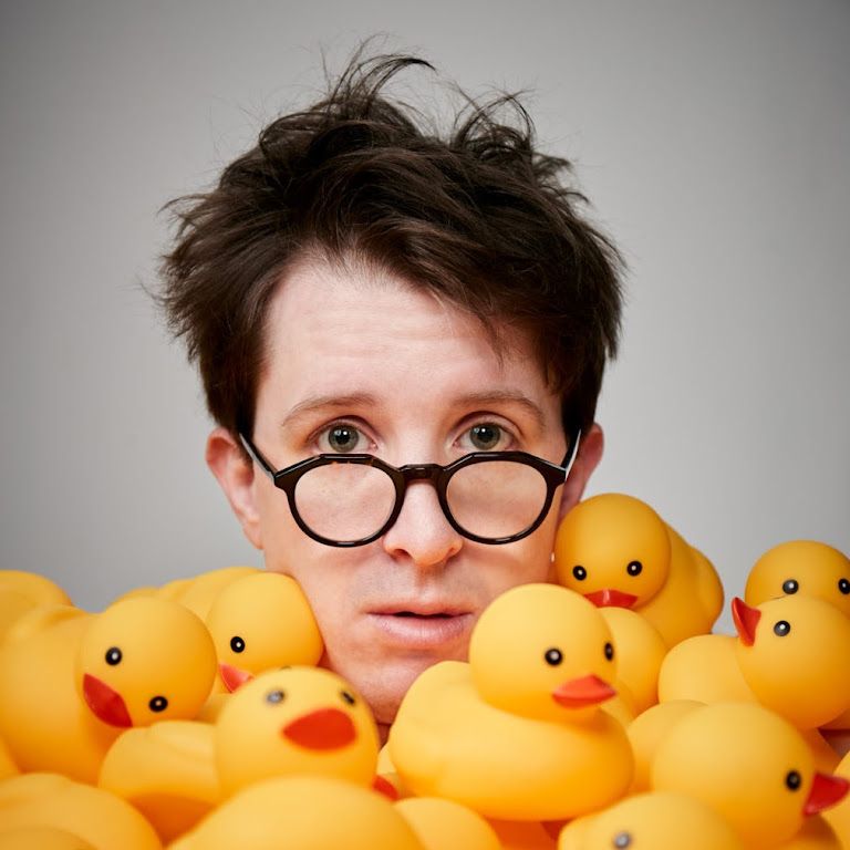 A headshot of comedian James Veitch surrounded by ducks