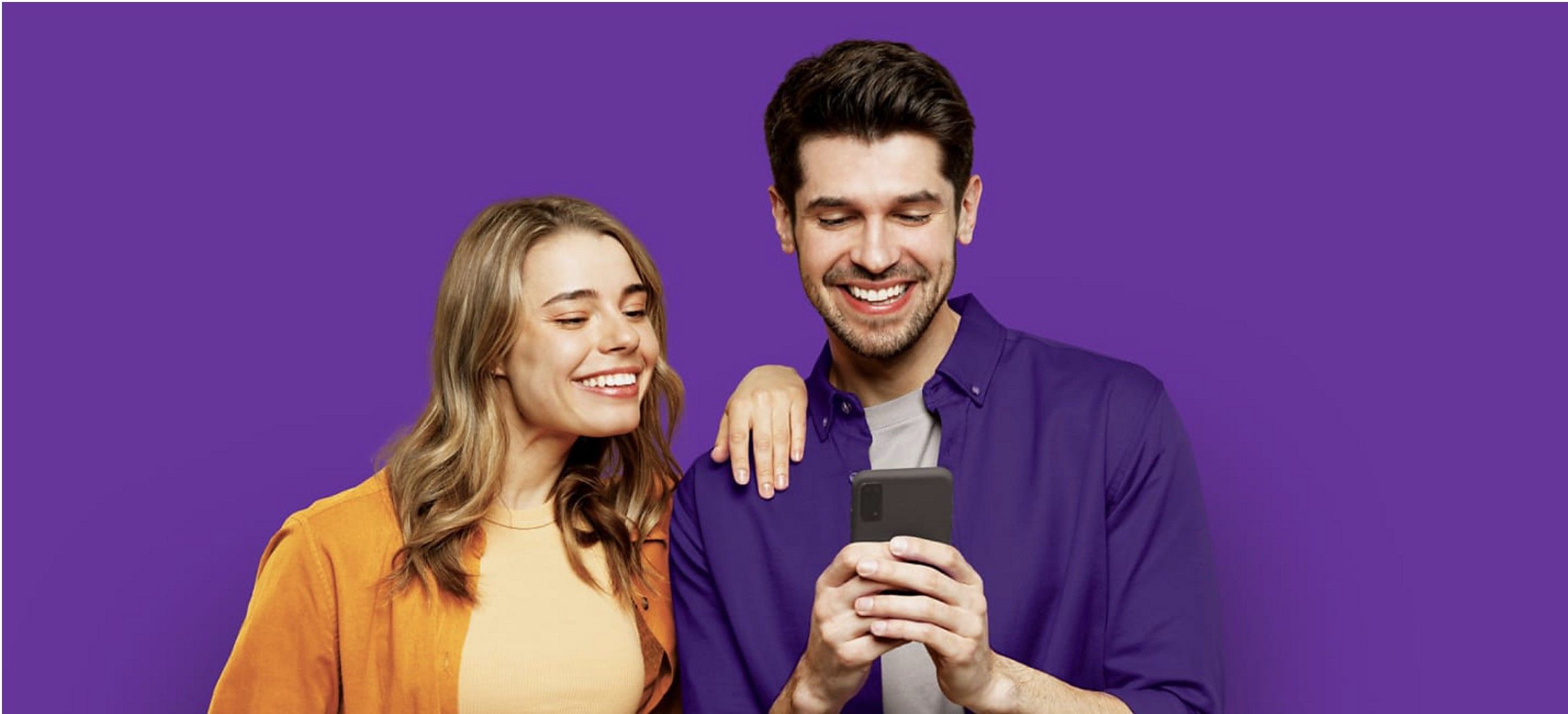 Two people smiling and holding phones while looking at one of the people's phones