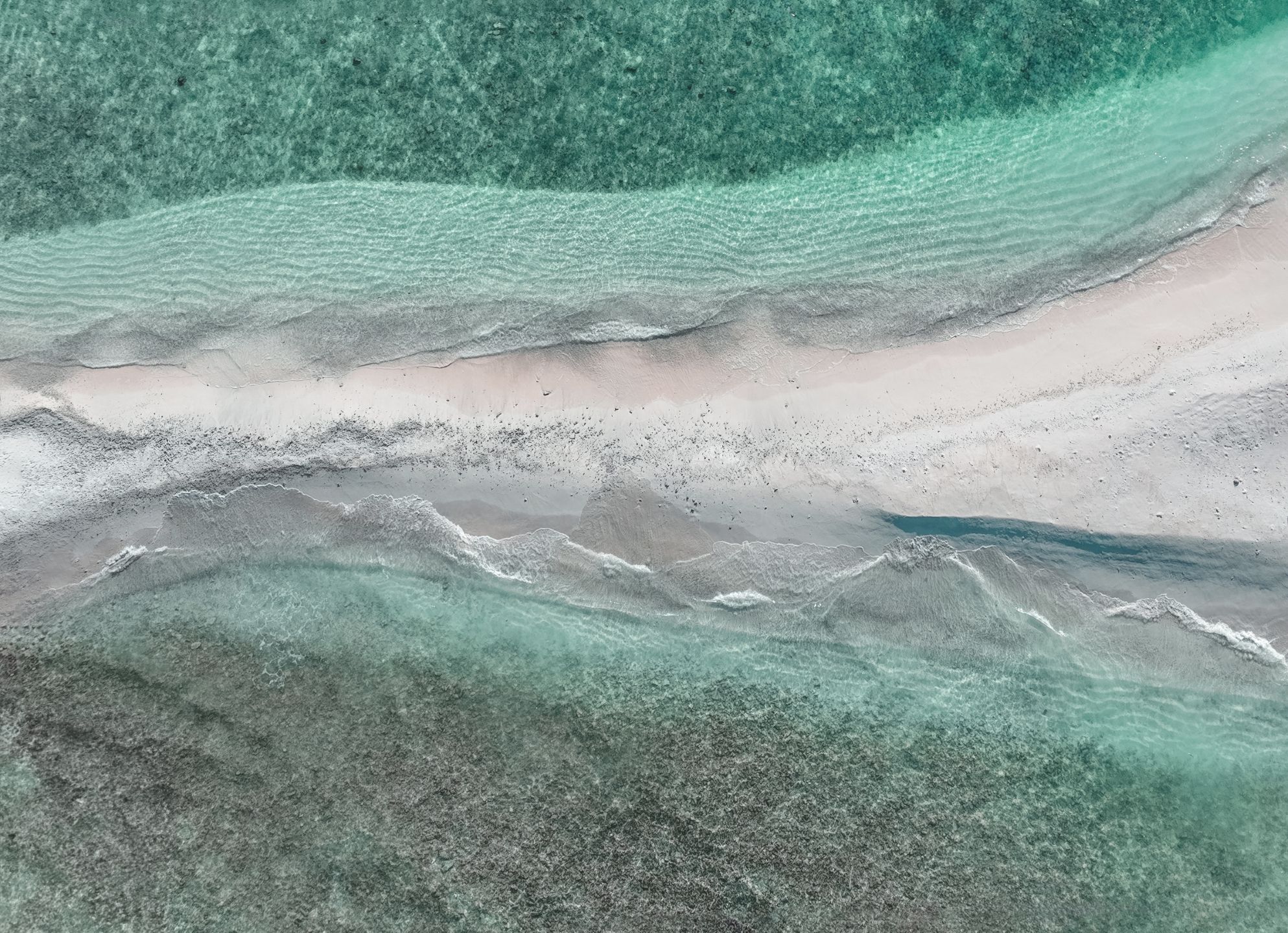 An aerial view of the Maldives white sand beaches with clear green water on either side 