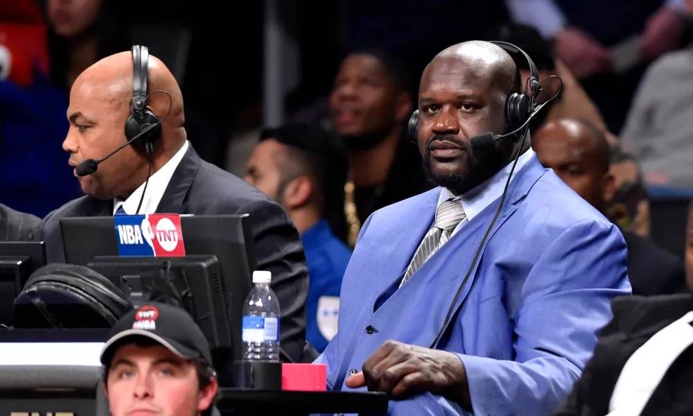 Shaquille O'Neal wearing a headset and sitting next to Charles Barkley at an NBA game