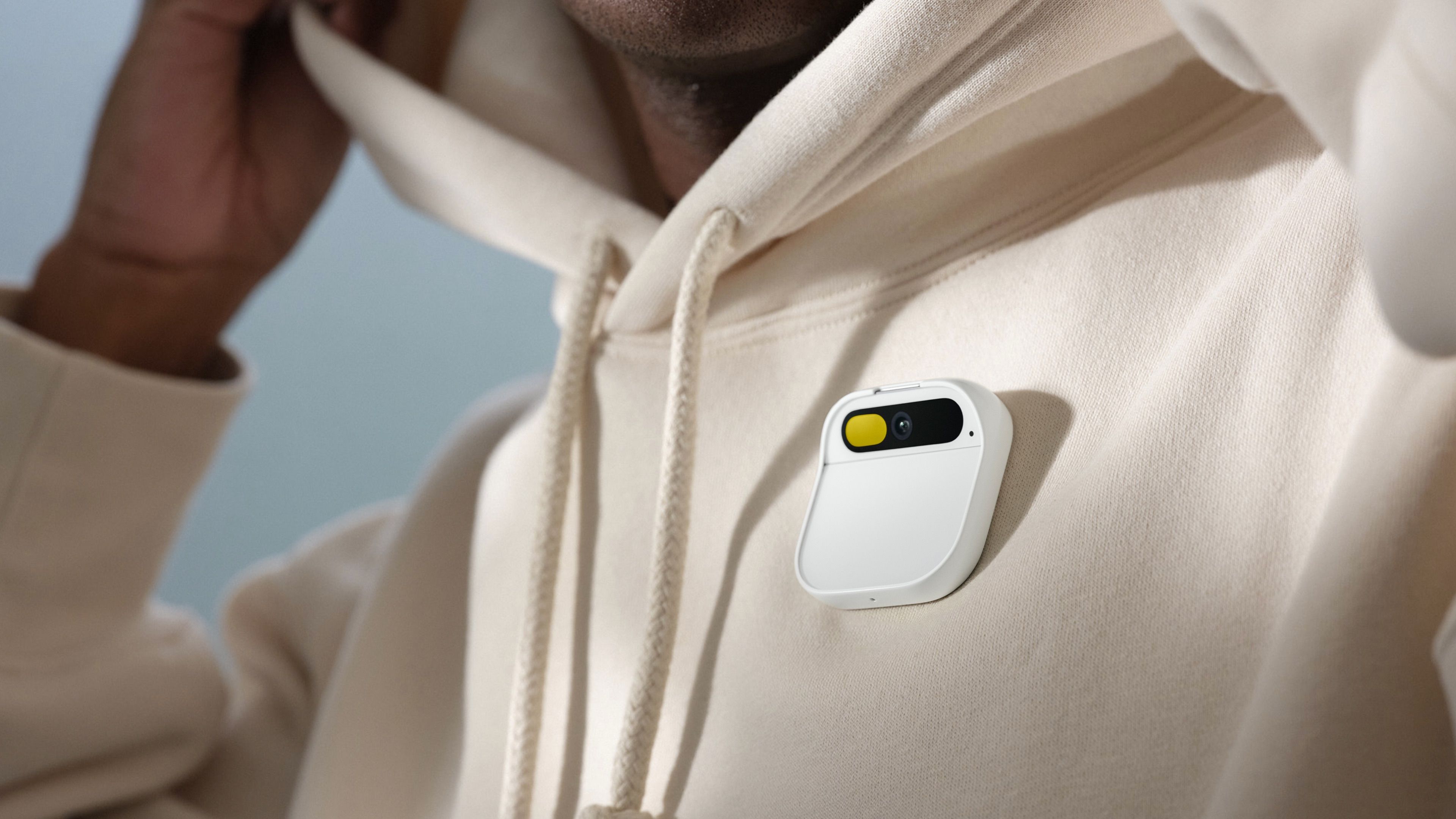 A white Humane AI Pin attached to a person's cream hoodie