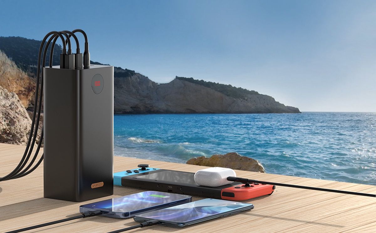 Romoss high-capacity portable charger sitting by a beach, charging a Nintendo Switch, AirPods, and two Android phones