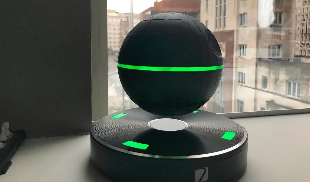 Hovering, glowing bluetooth speaker sitting on a desk in front of a window that looks out to the city