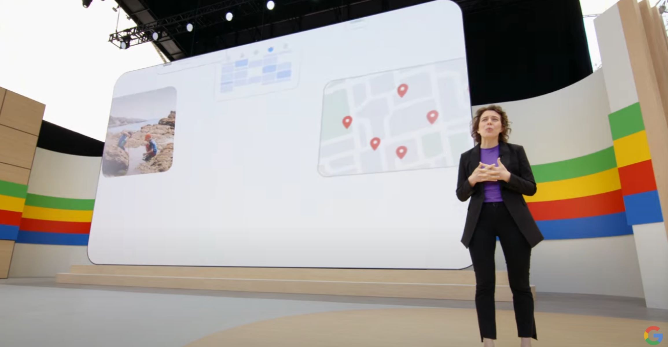 A screenshot of Liz Reid standing on stage at Google IO with a screen behind her displaying a map and a photo.