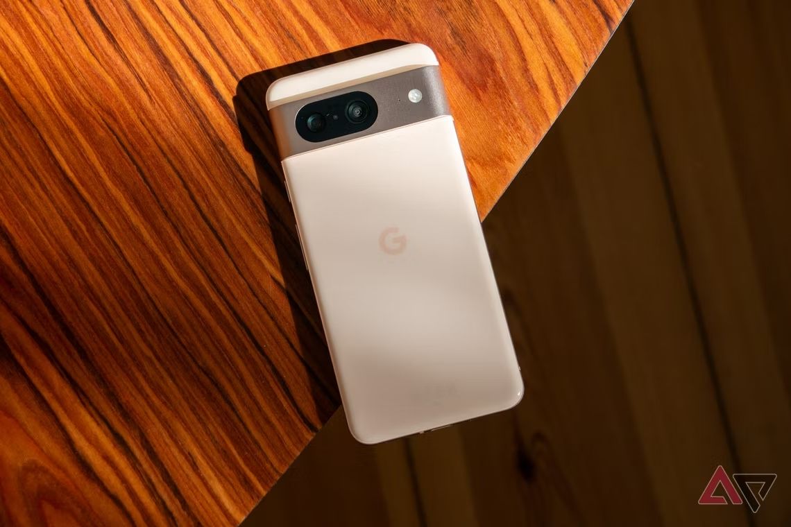 A white Google Pixel 8 laying face-down on a wooden table.