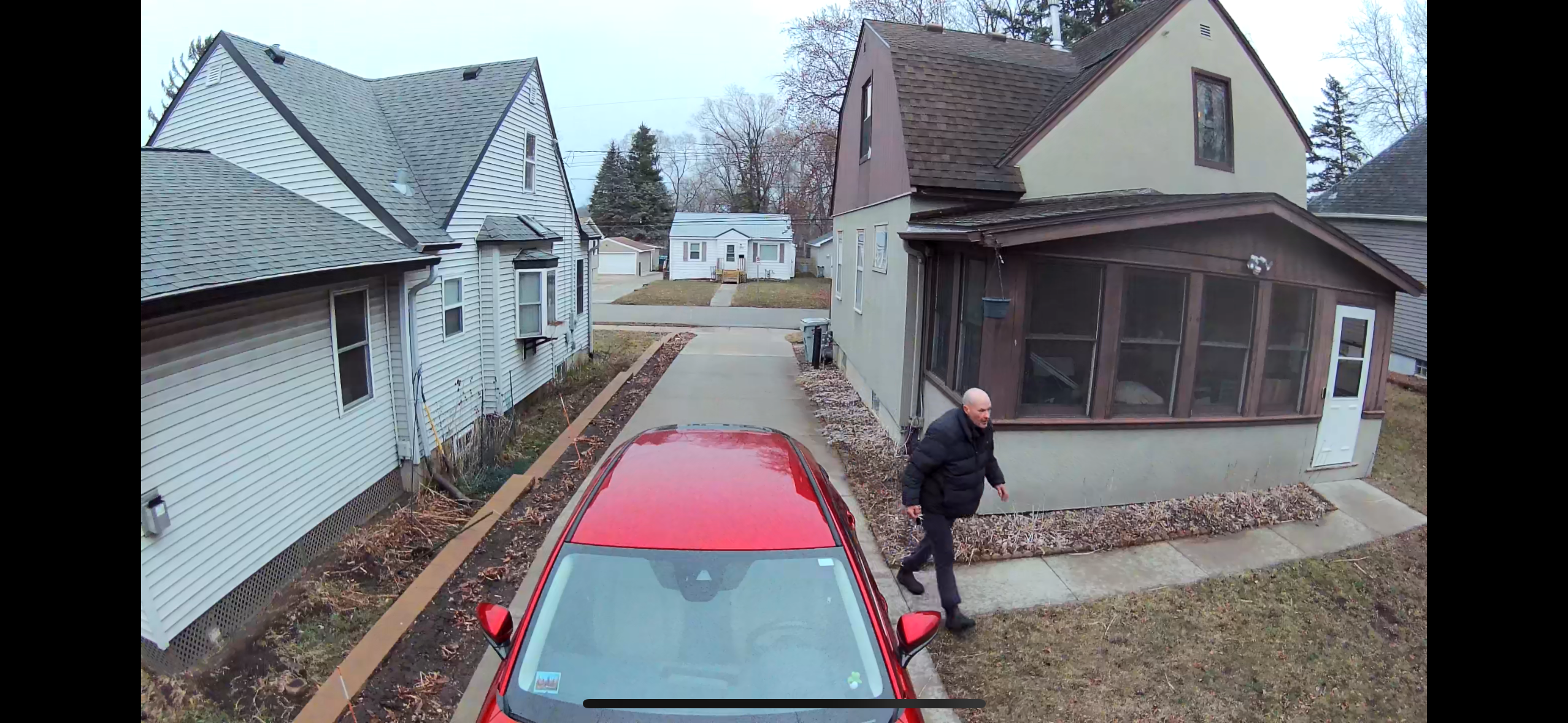 Man walking across driveway by home and red car