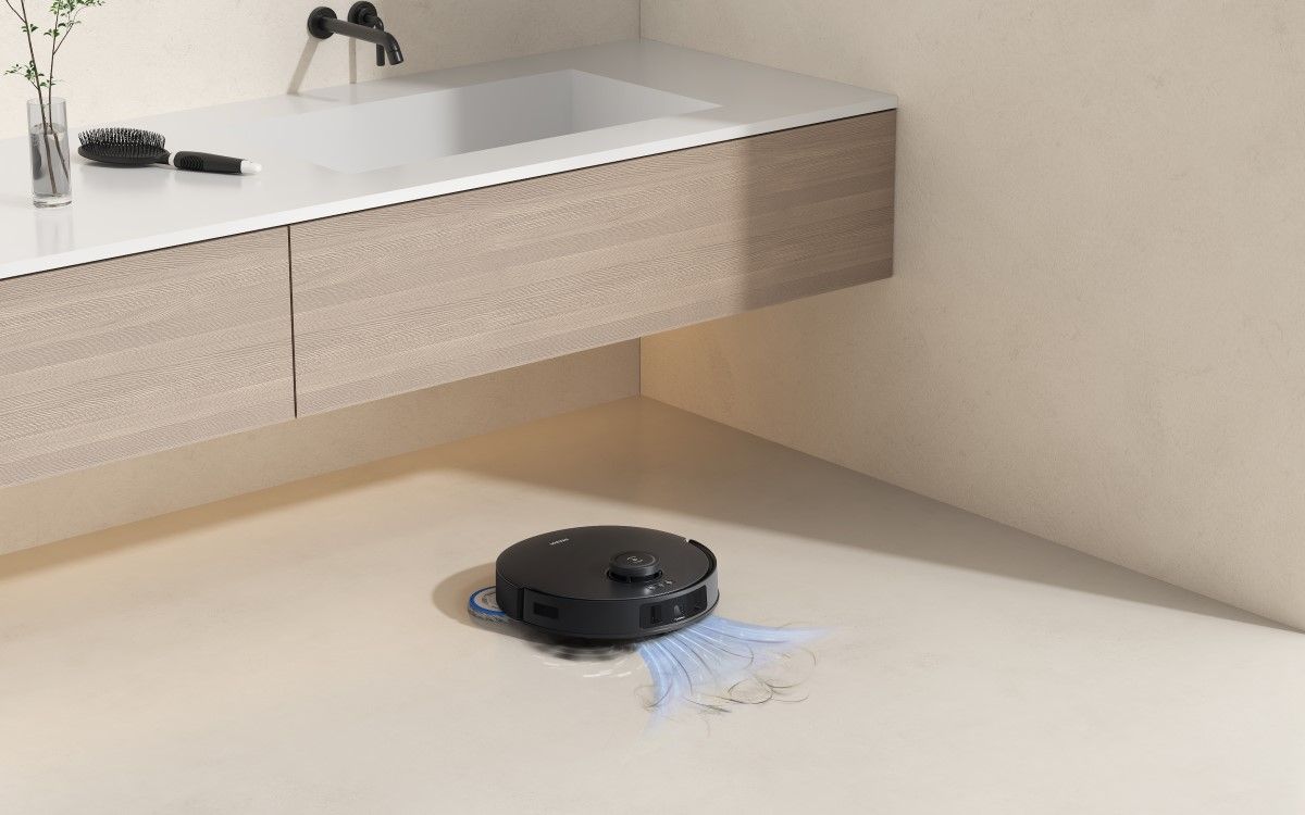 A black robot vacuum sucks up hair on a beige floor