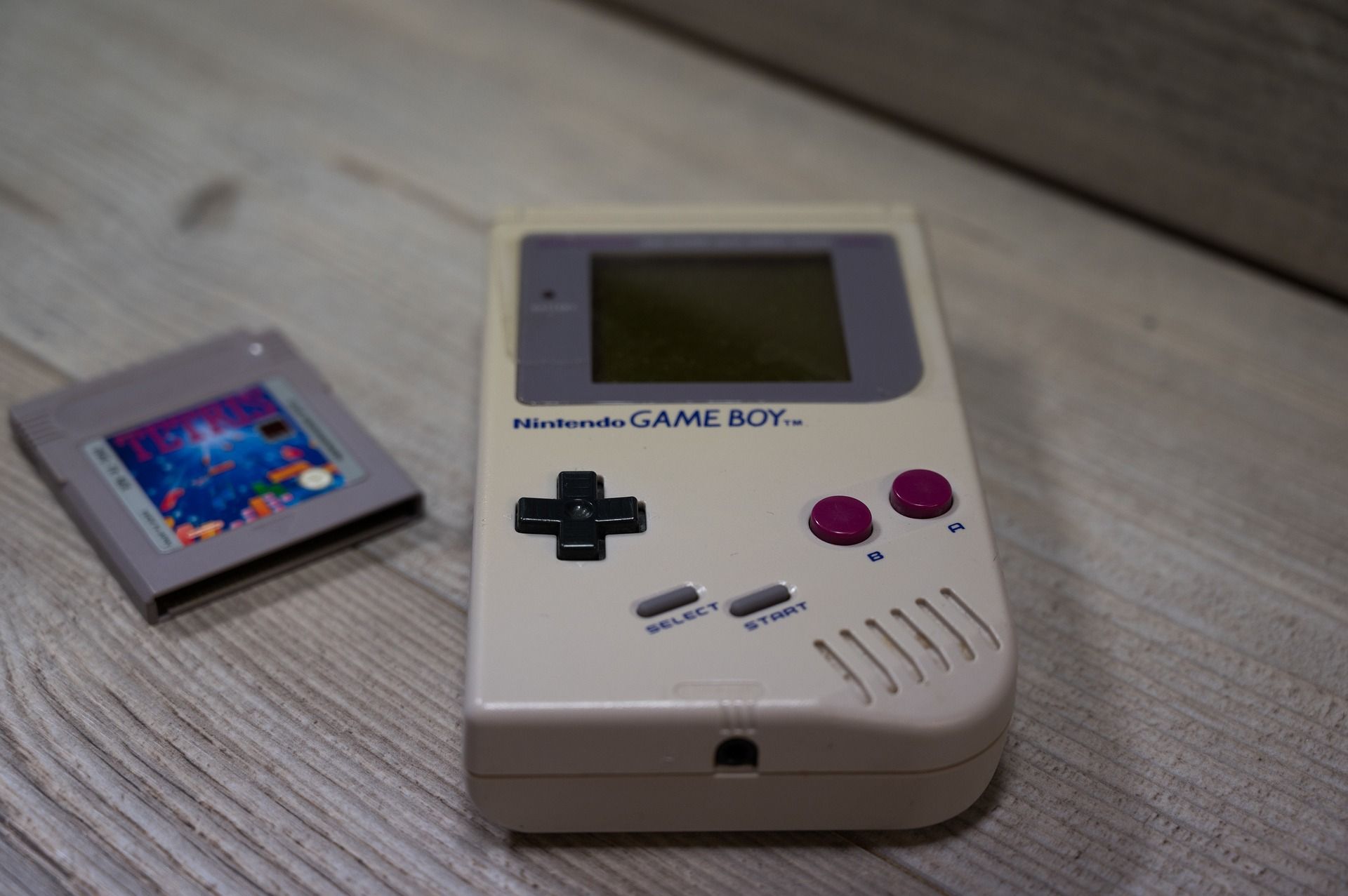 A Nintendo Game Boy laying on a table next to a Tetris game cartridge.